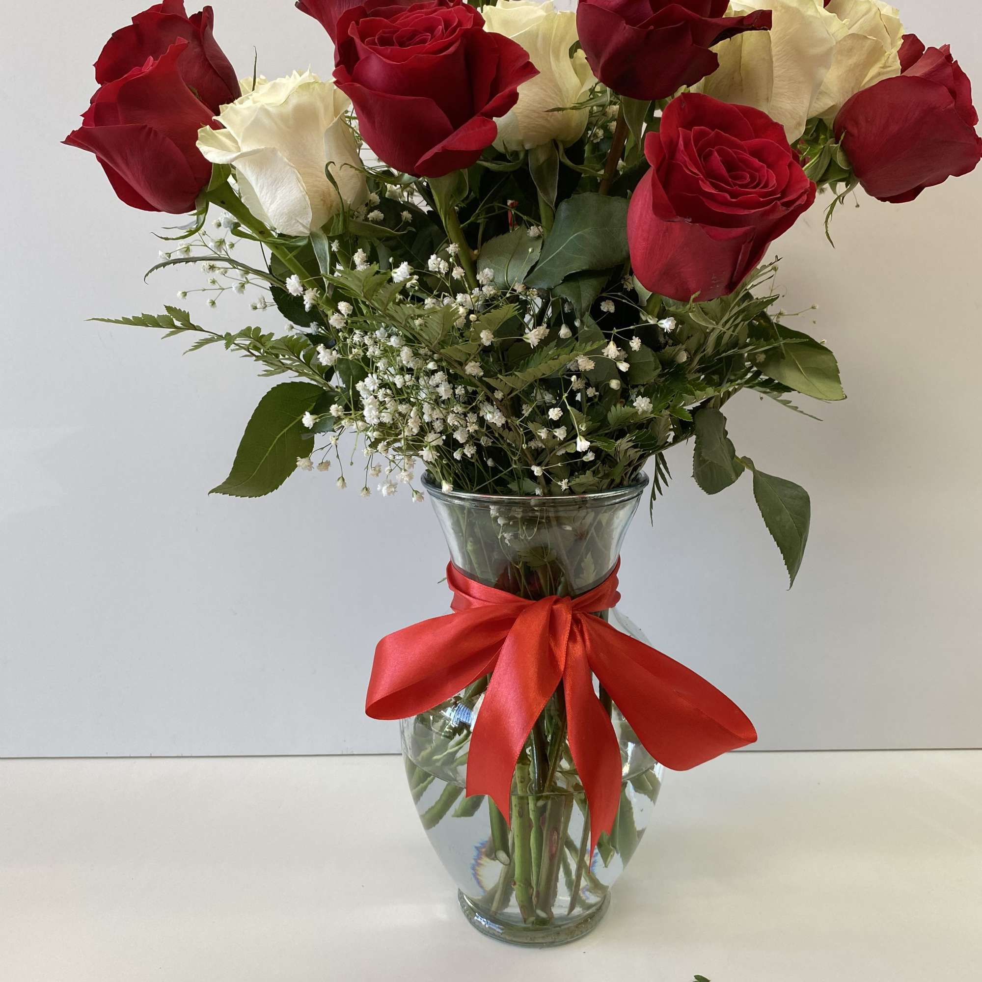 Arrangement of red and white roses with baby’s breath in a clear vase tied with a red ribbon