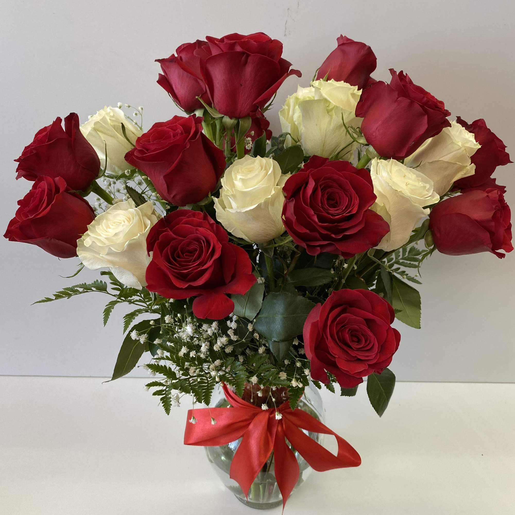 Arrangement of red and white roses with filler flowers in a clear glass vase with a red bow