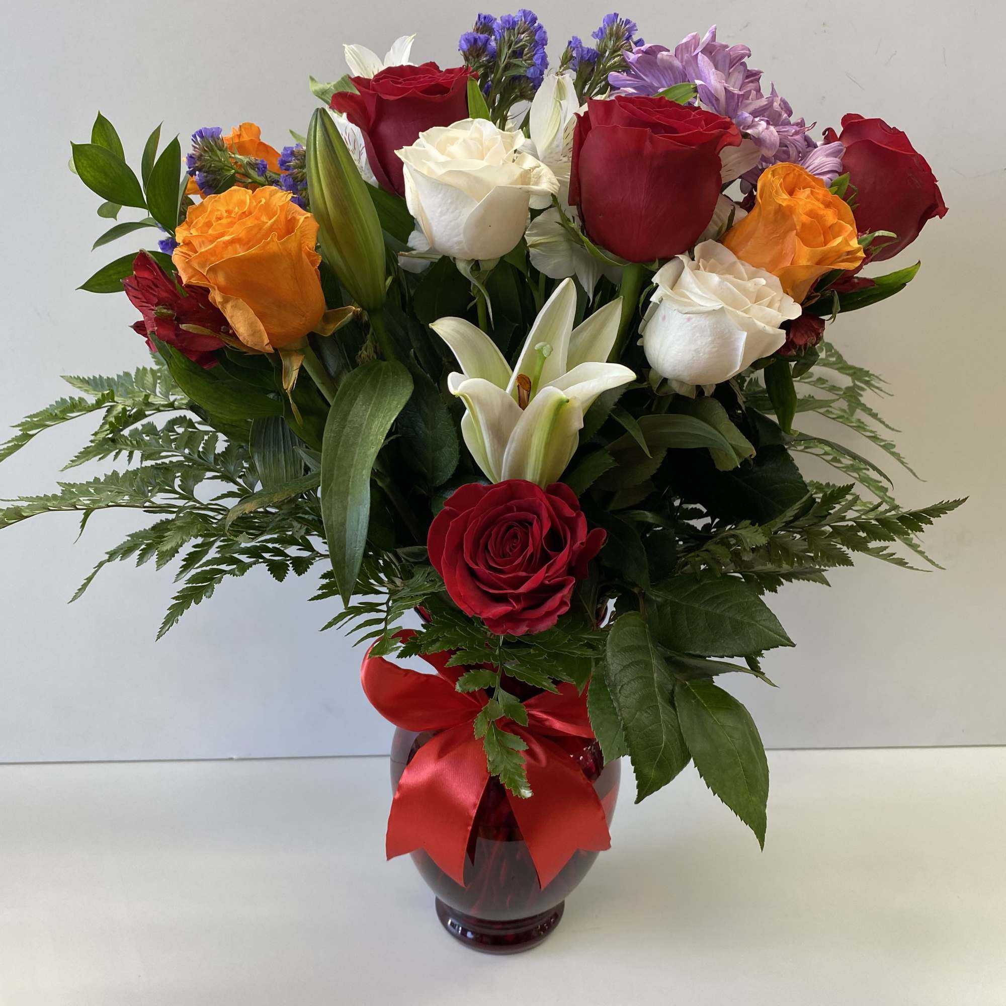Bouquet of red, white, and orange roses in a glass vase with a red ribbon
