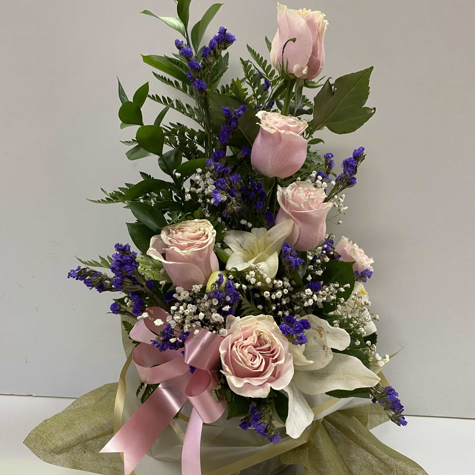 Pink roses and white lilies arranged with purple filler in a vase