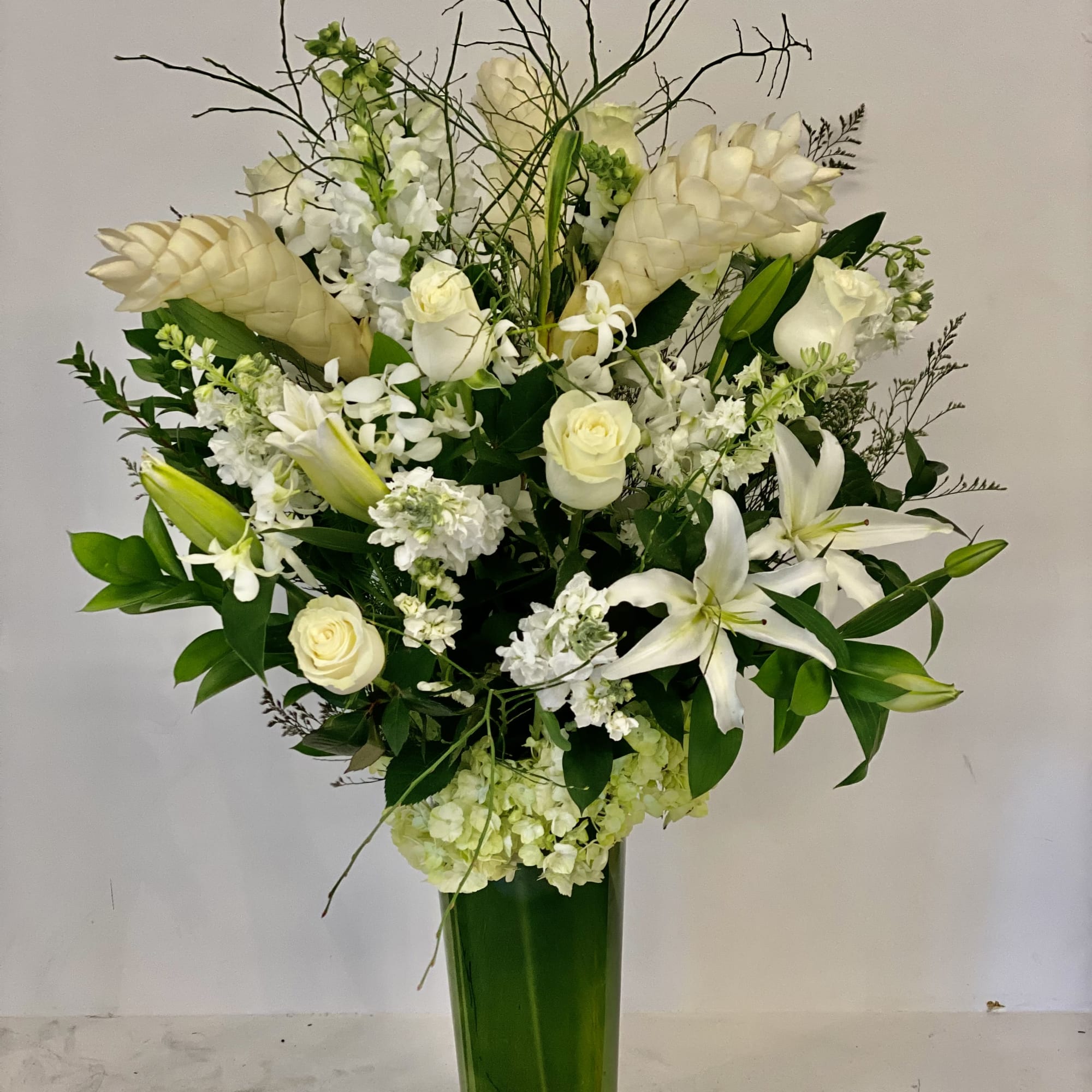 White floral arrangement in a tall green vase with lilies and roses
