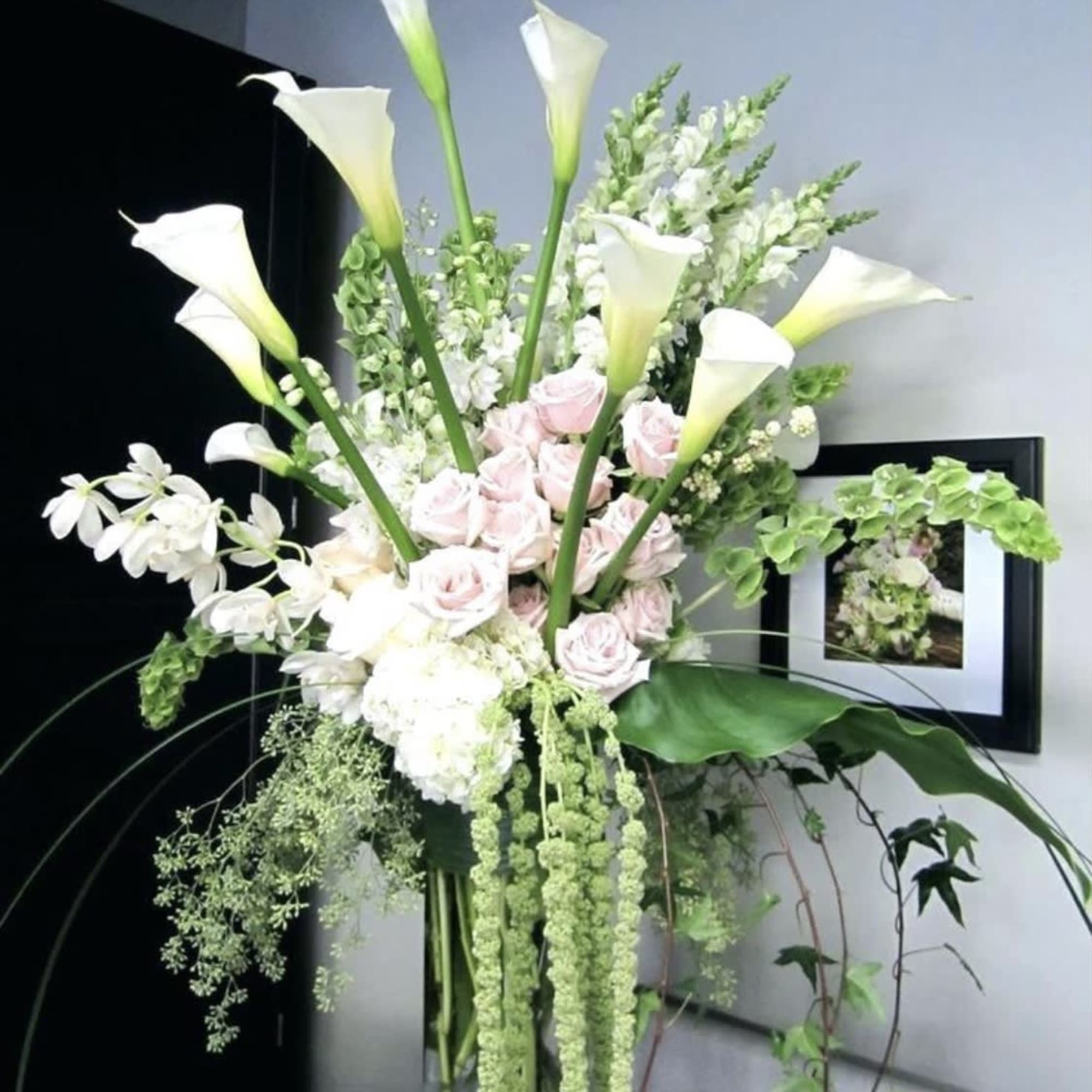 Tall arrangement of white calla lilies and pale pink roses in a glass vase