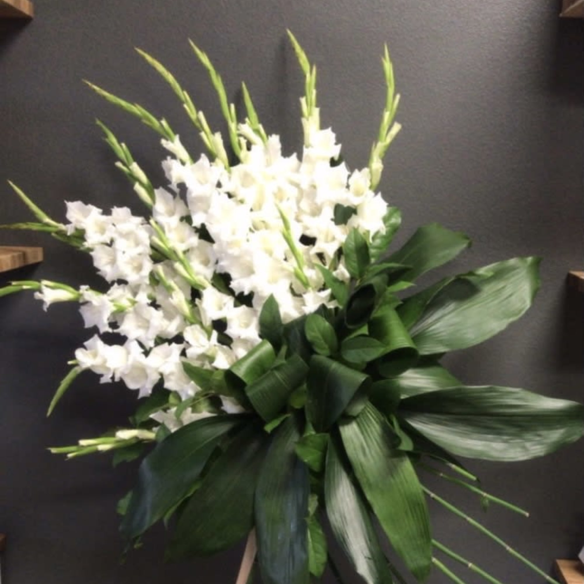 White gladiolus arrangement with broad green leaves on an easel