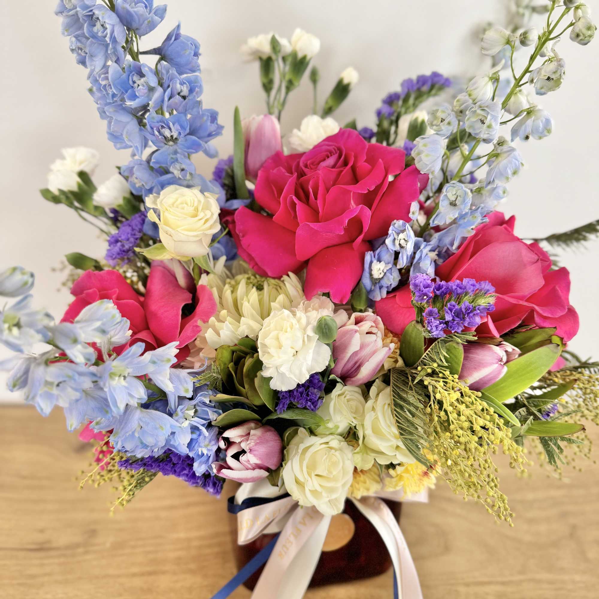 Mixed bouquet of pink roses, blue delphinium, and white blooms in a vase