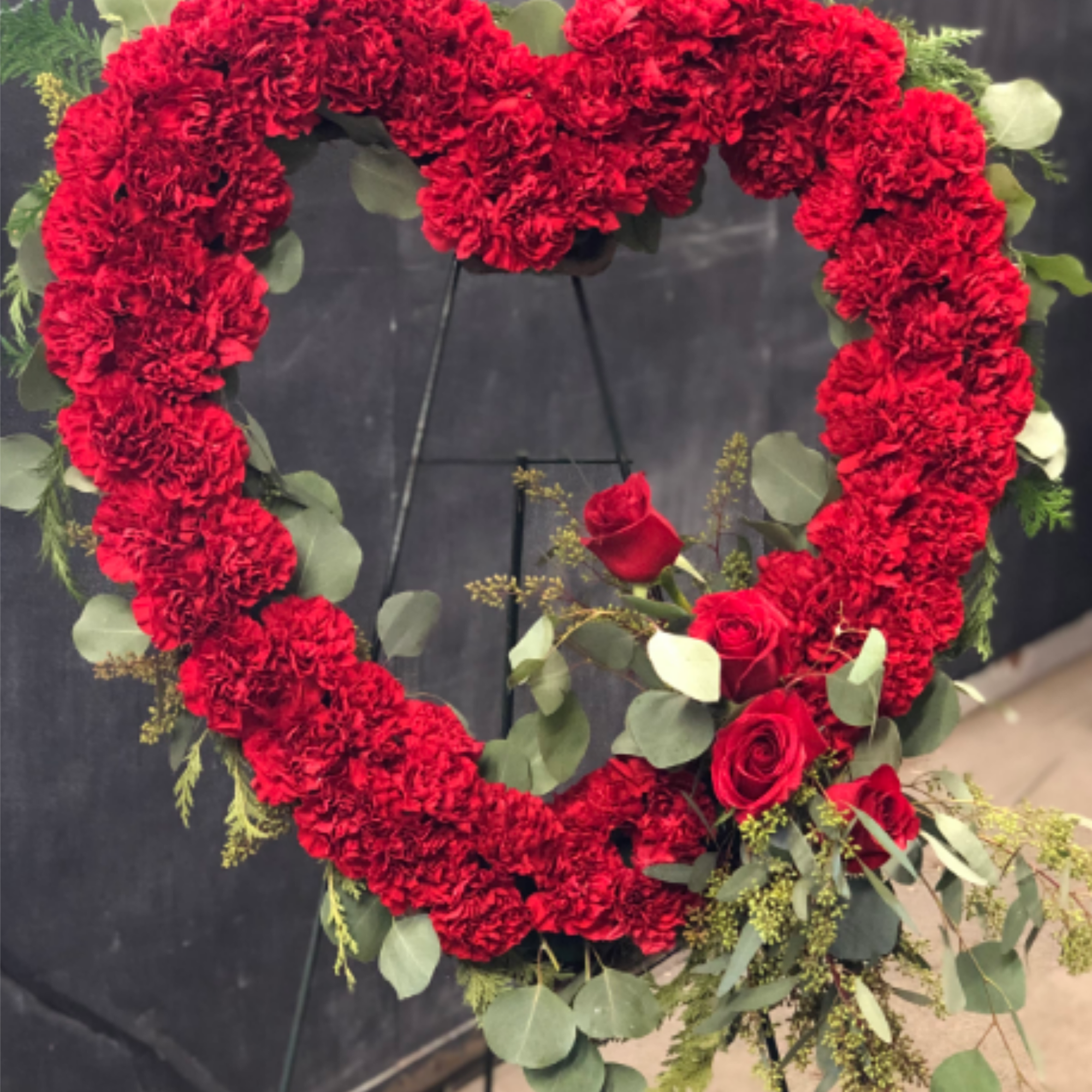 A bold heart of densely packed red carnations-accented with a cluster of