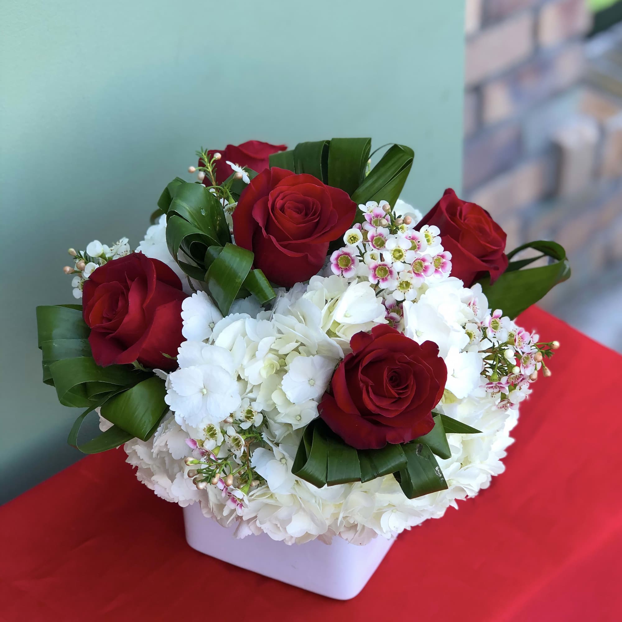 Red roses and white hydrangeas in a white square vase