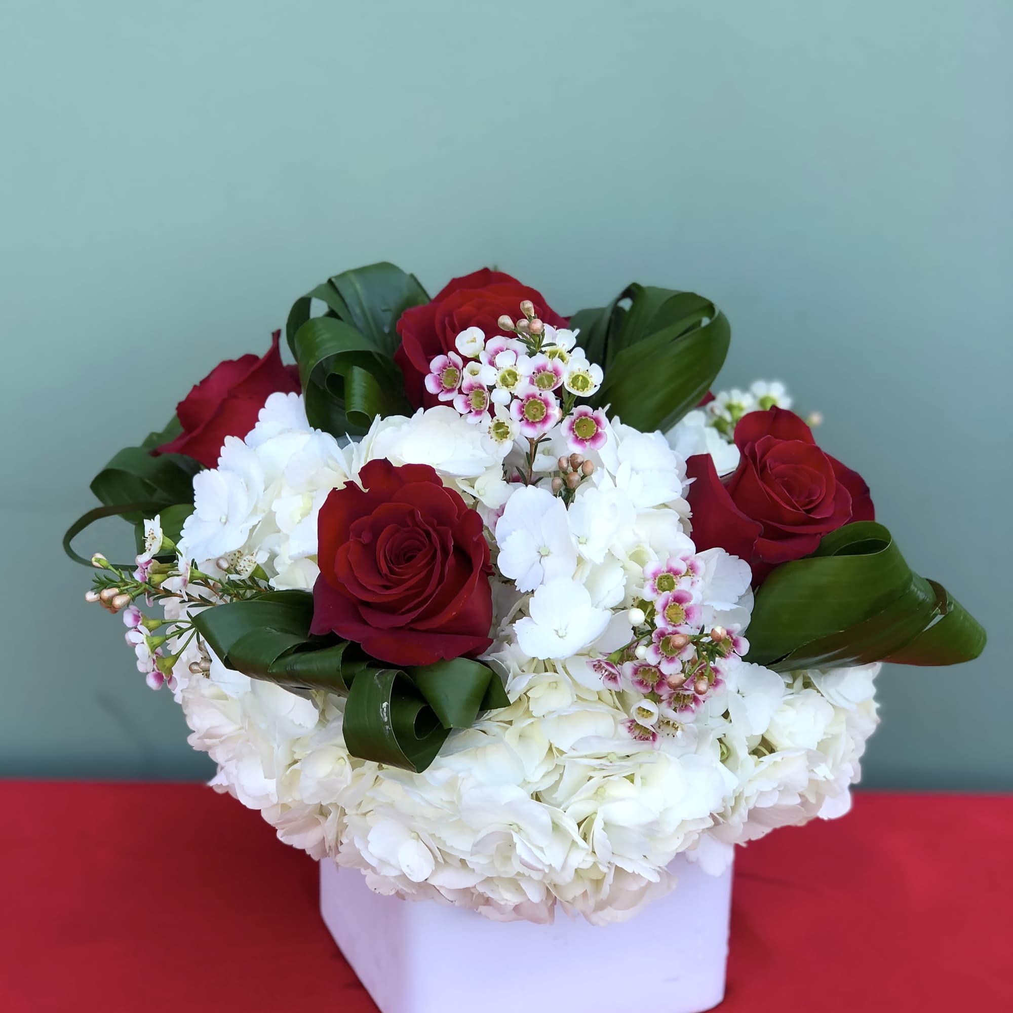 Red roses and white hydrangeas in a white square vase