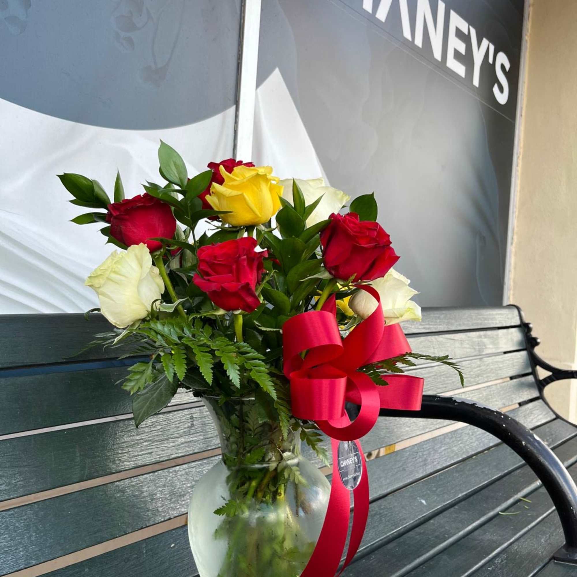 Bouquet of red, yellow, and white roses in a glass vase with a red ribbon