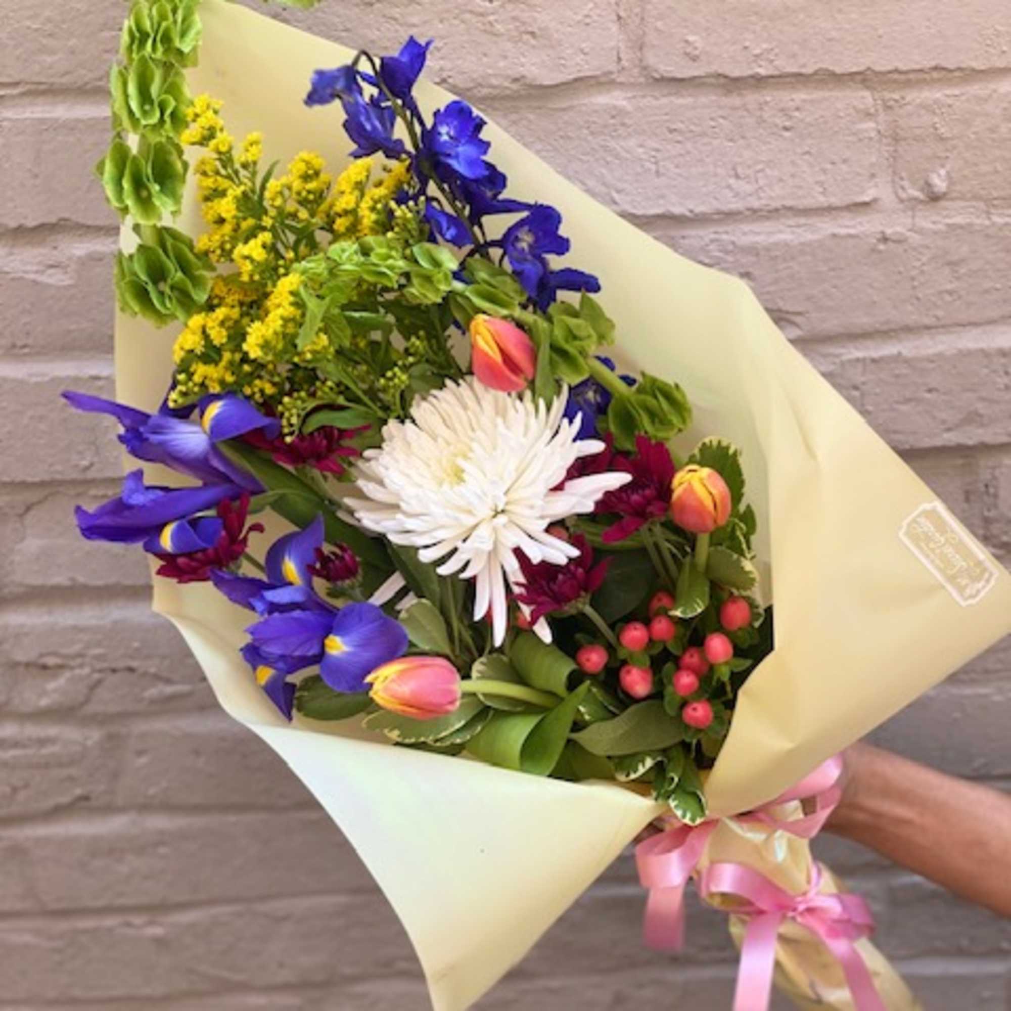 Colorful mixed bouquet wrapped in pale paper with a pink ribbon