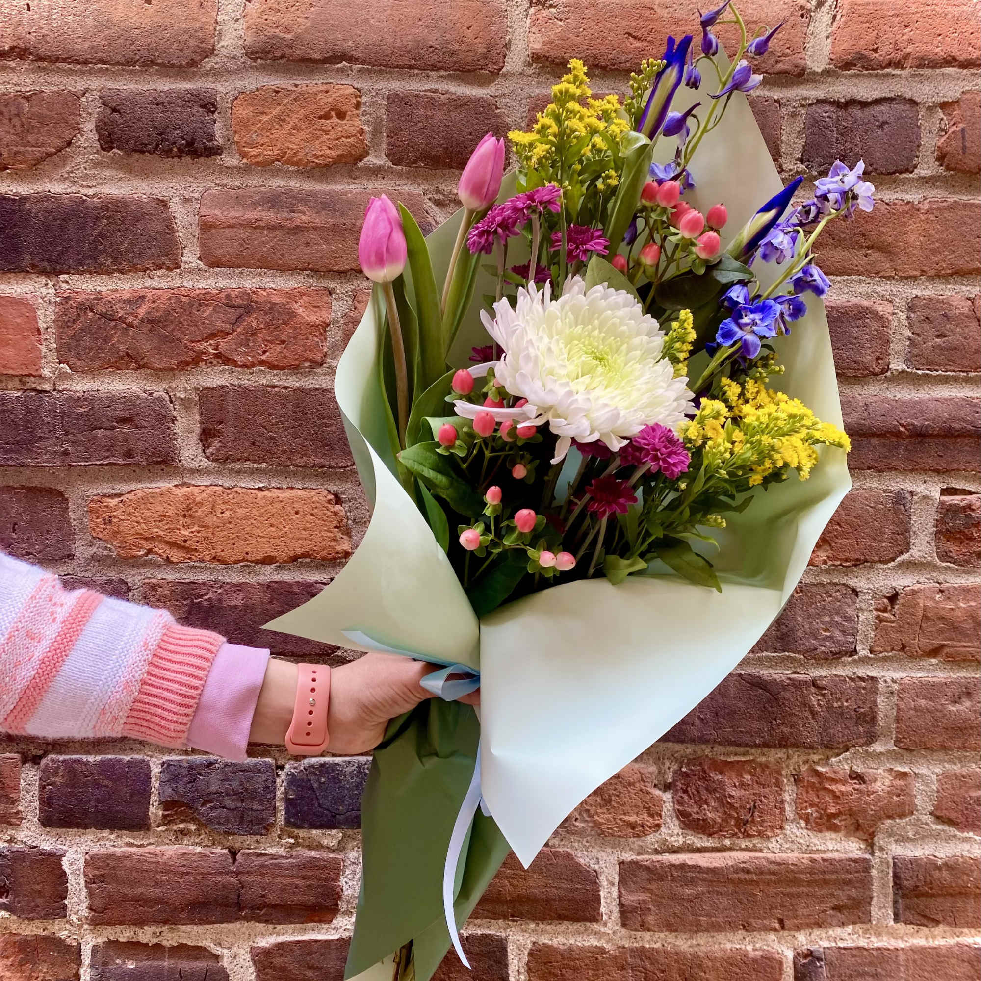 Handheld bouquet of pink tulips, white chrysanthemum, and purple flowers