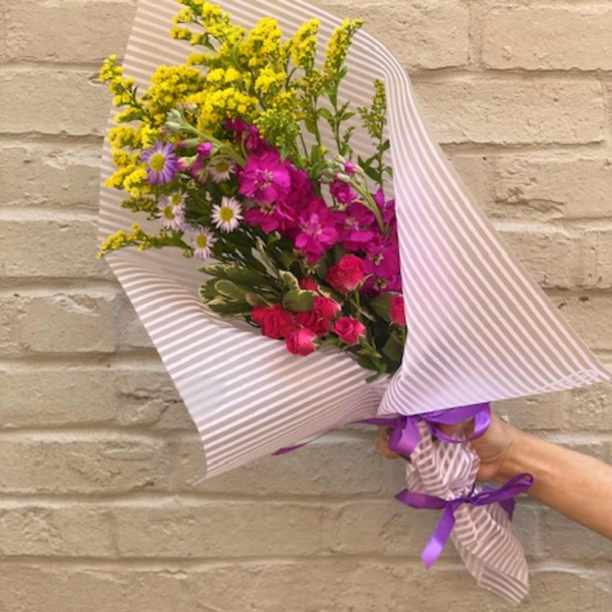 Hand-tied bouquet of pink and yellow flowers wrapped in striped paper