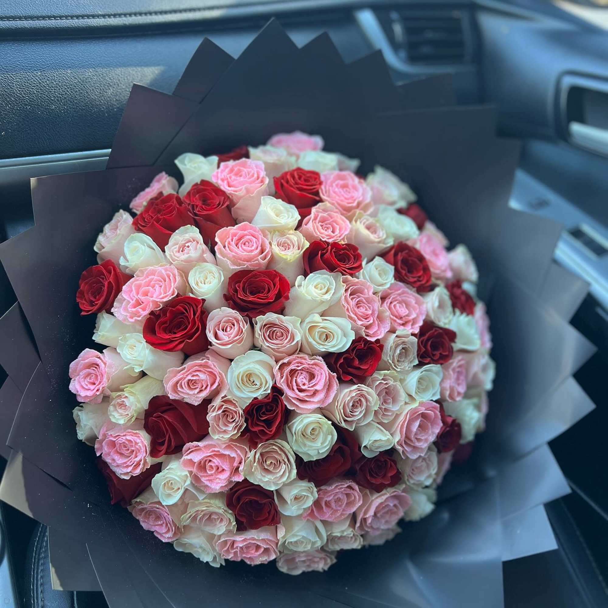 Round bouquet of pink, red, and white roses wrapped in black paper