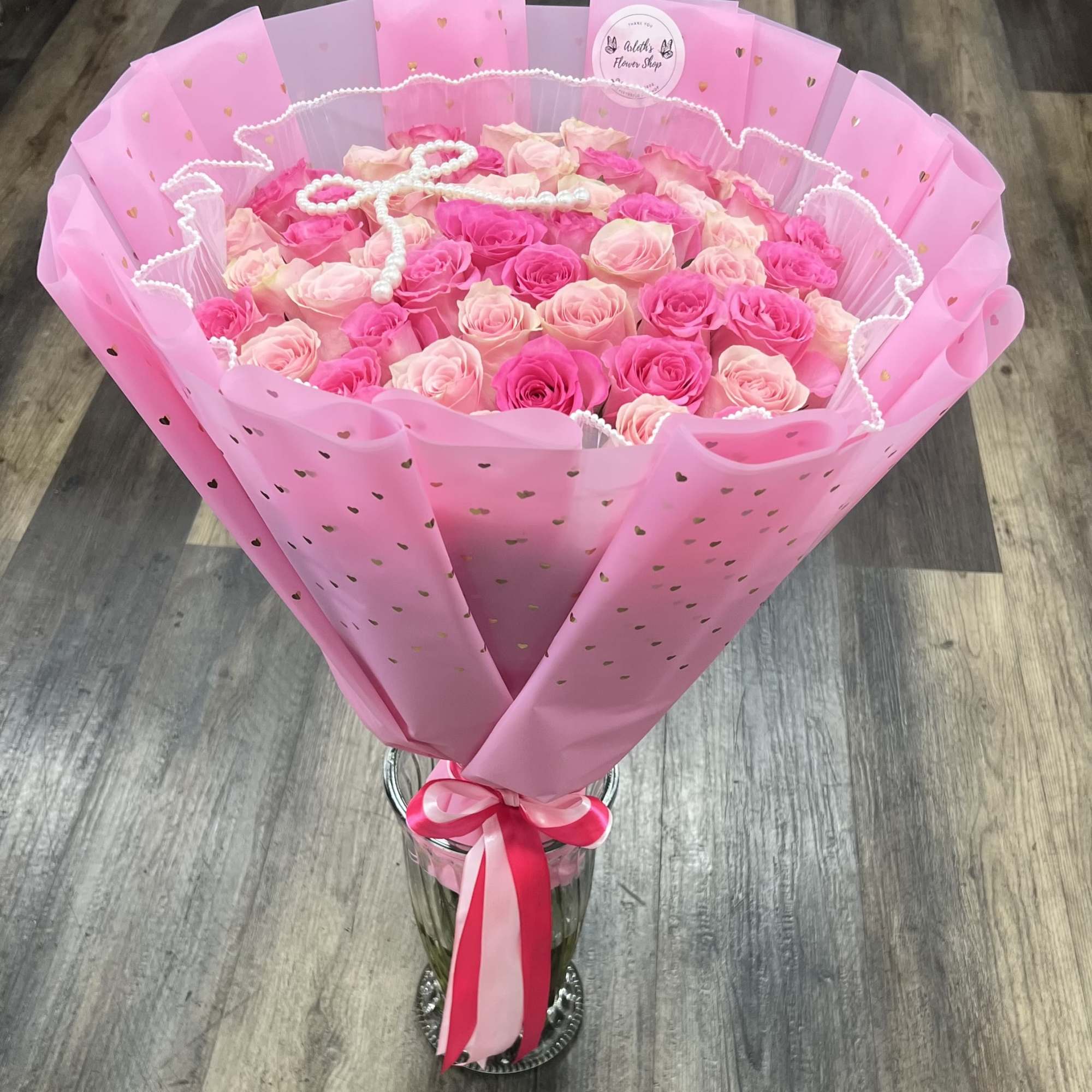 Pink and blush rose bouquet wrapped in pink paper with a ribbon, in a glass vase