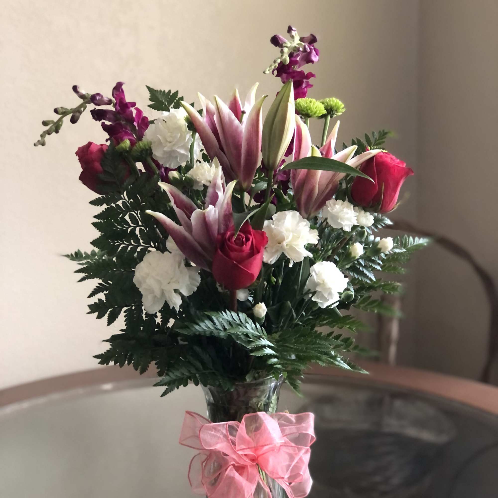 Bouquet of pink lilies, red roses, and white carnations in a glass vase with a pink ribbon