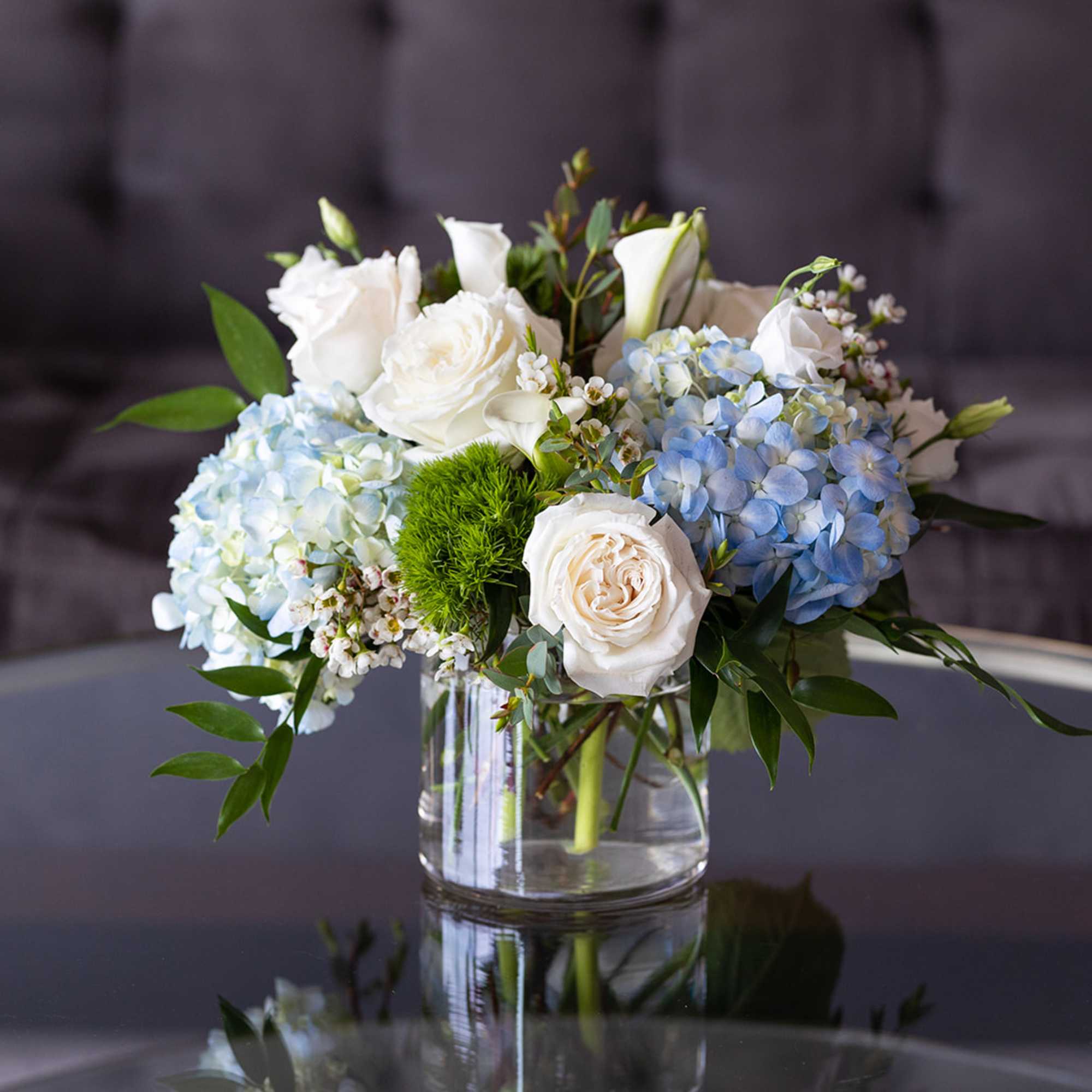 White roses and blue hydrangeas arranged in a clear glass vase