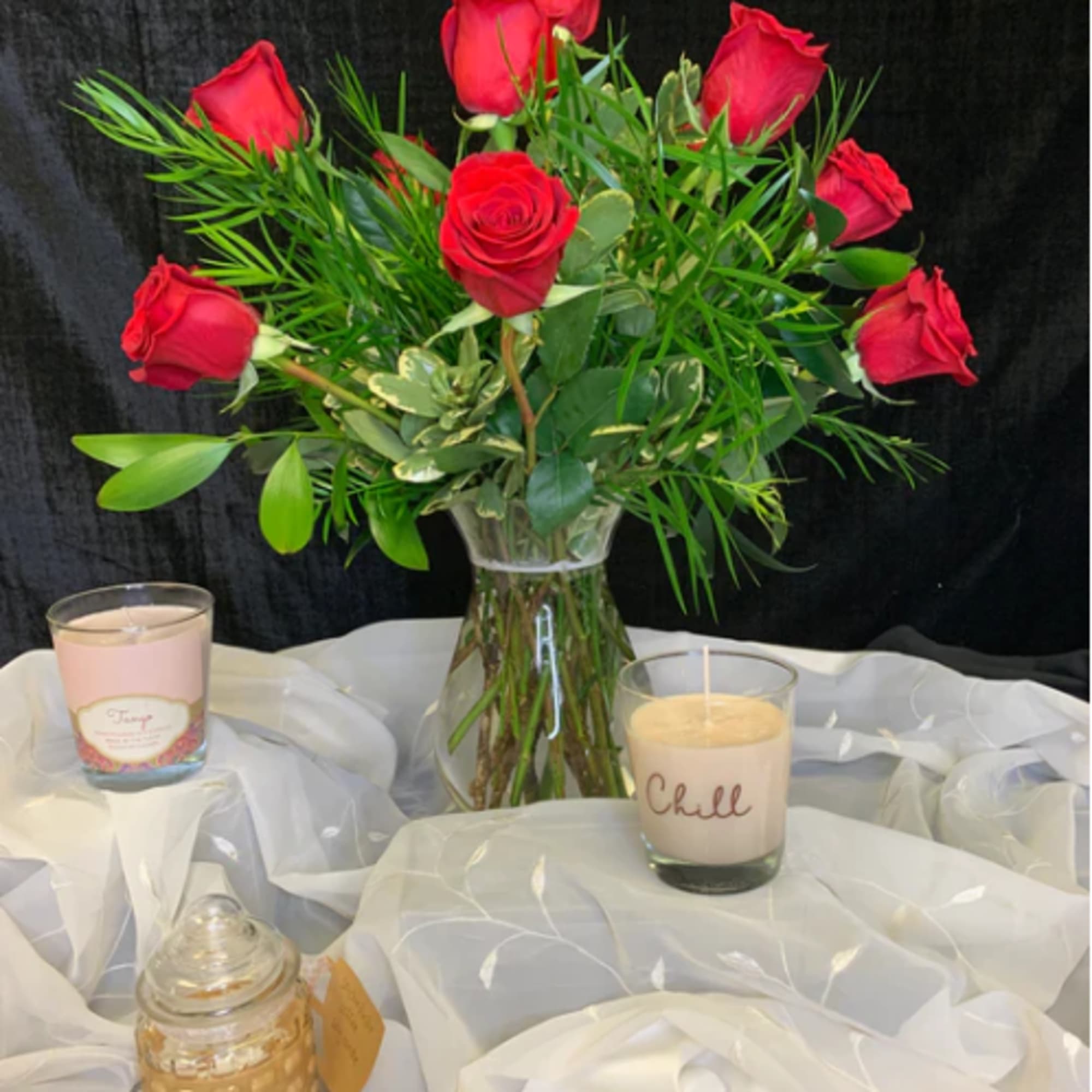 Red roses in a clear glass vase with candles on white fabric
