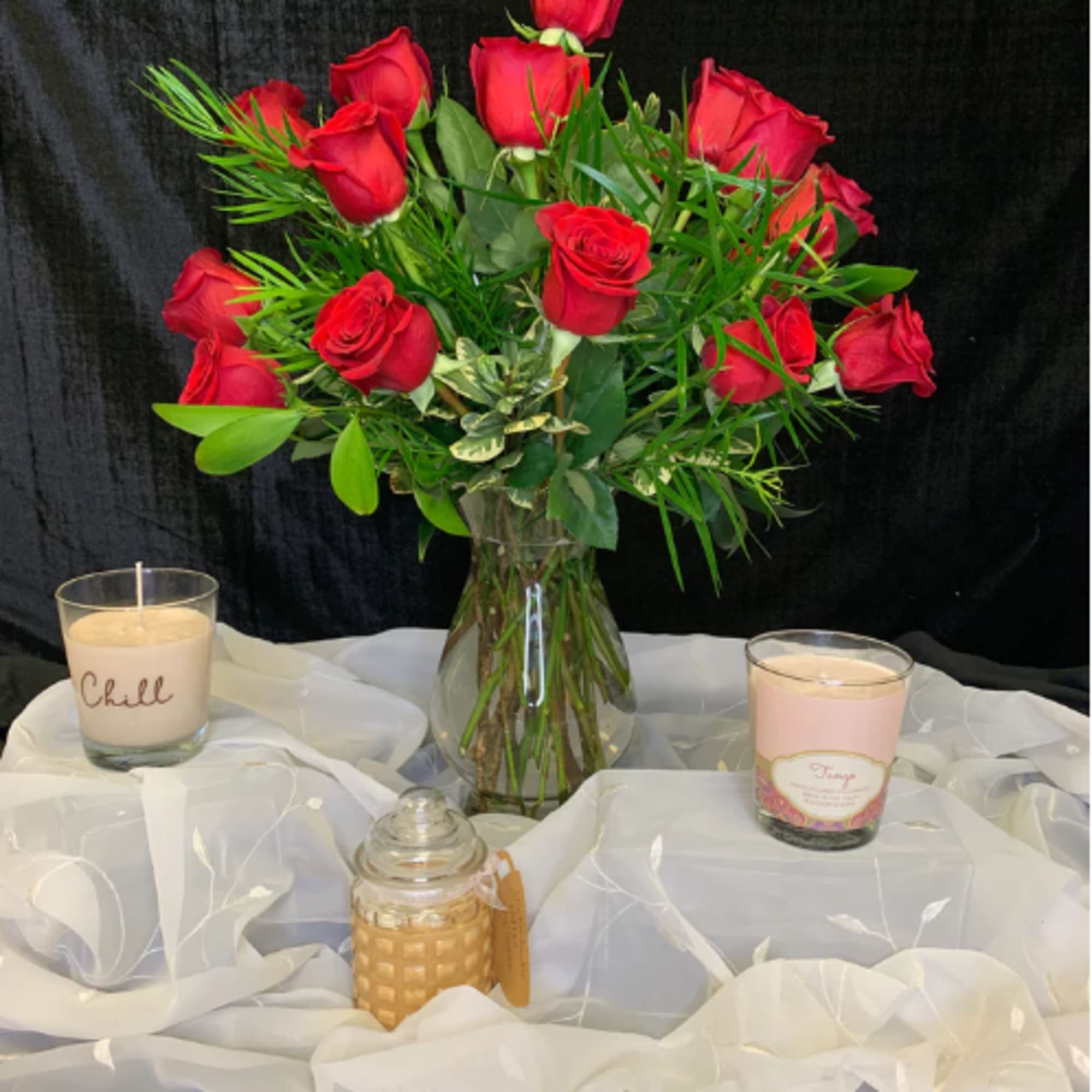 Red roses in a clear glass vase with candles on a draped table