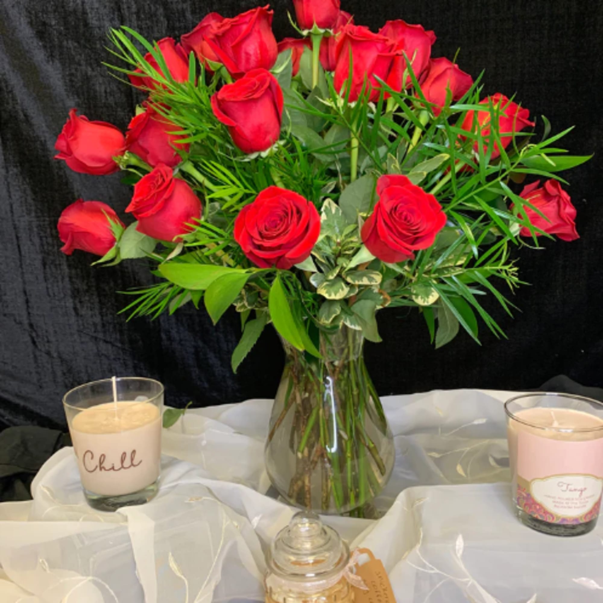 Bouquet of red roses in a clear glass vase with candles nearby