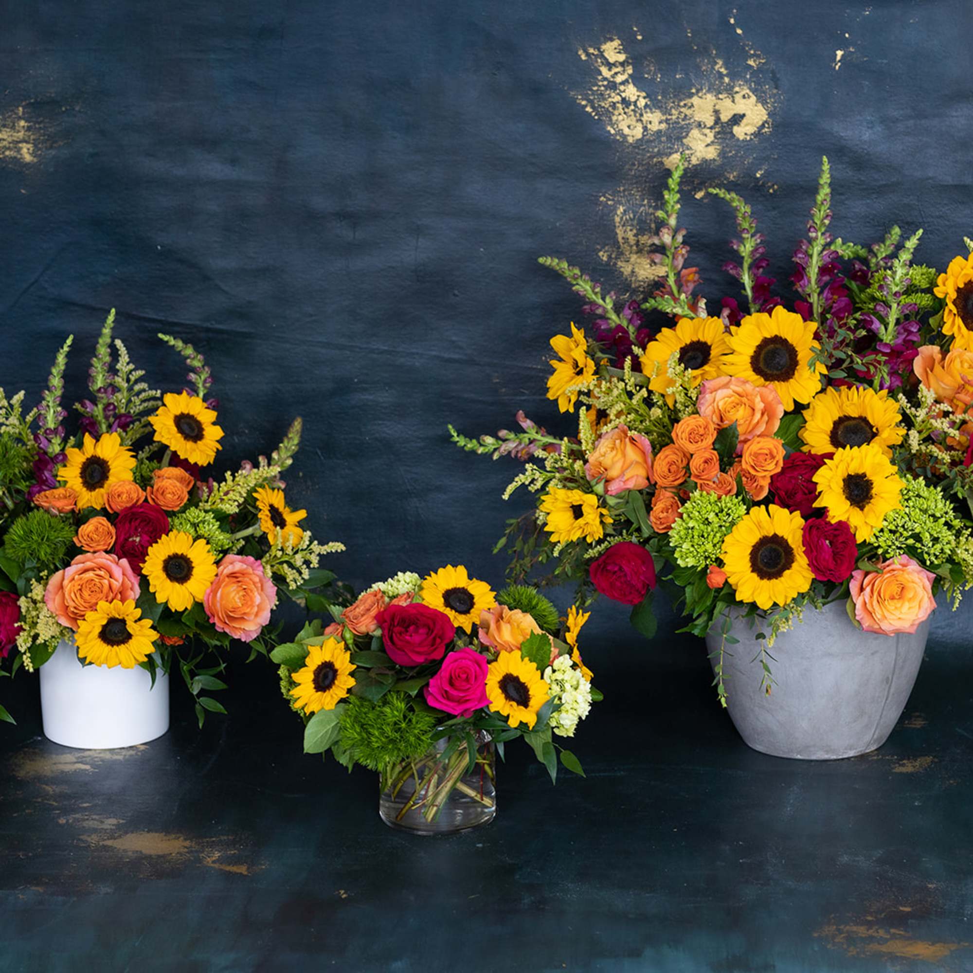 Three floral arrangements with sunflowers and roses in vases