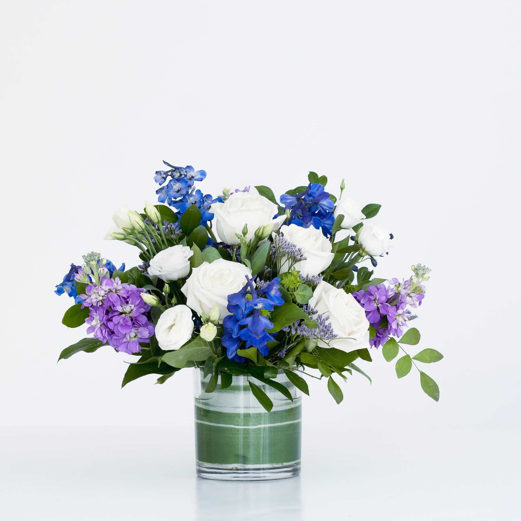 Low glass vase arrangement of white roses with blue and purple flowers