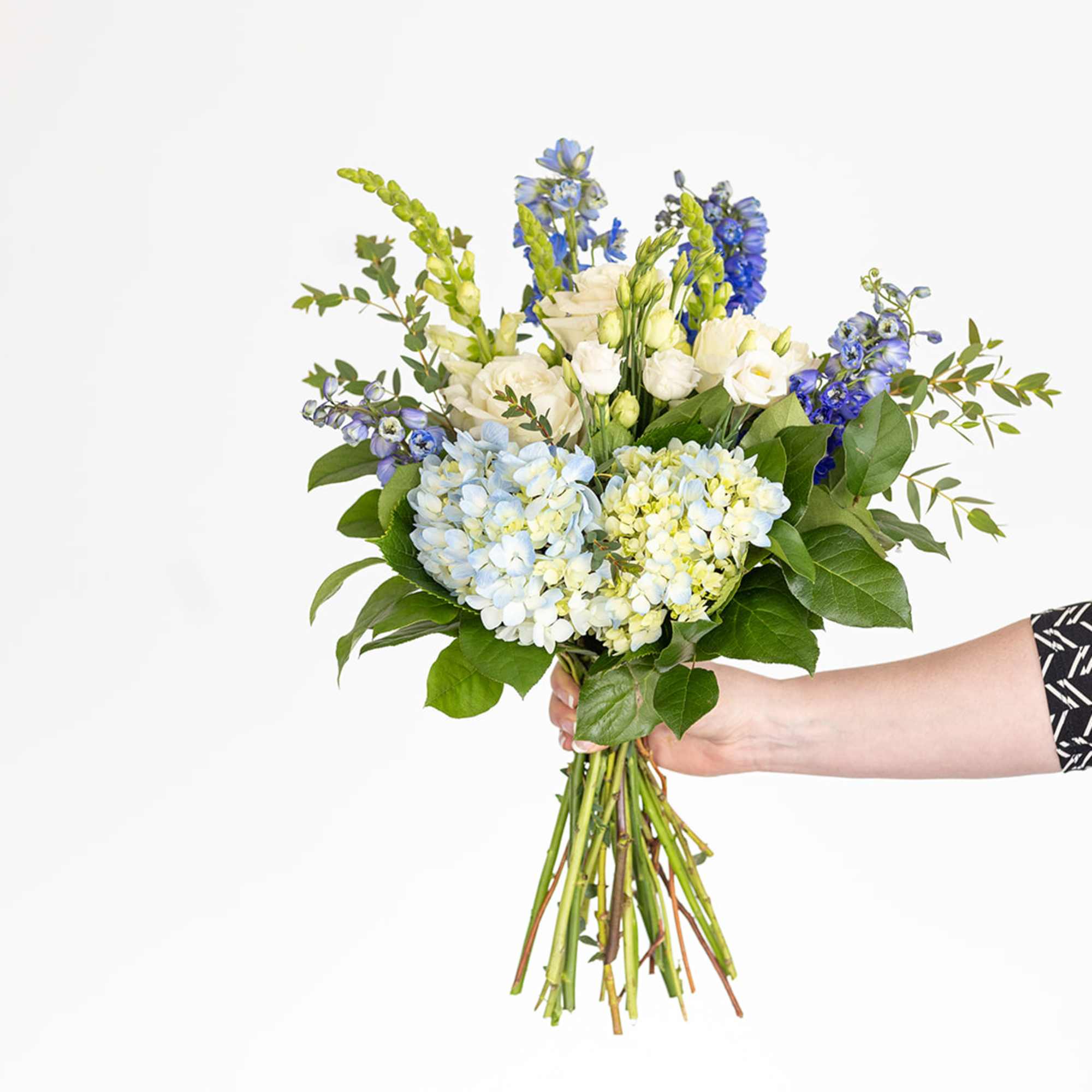 Handheld bouquet of blue and white flowers with greenery