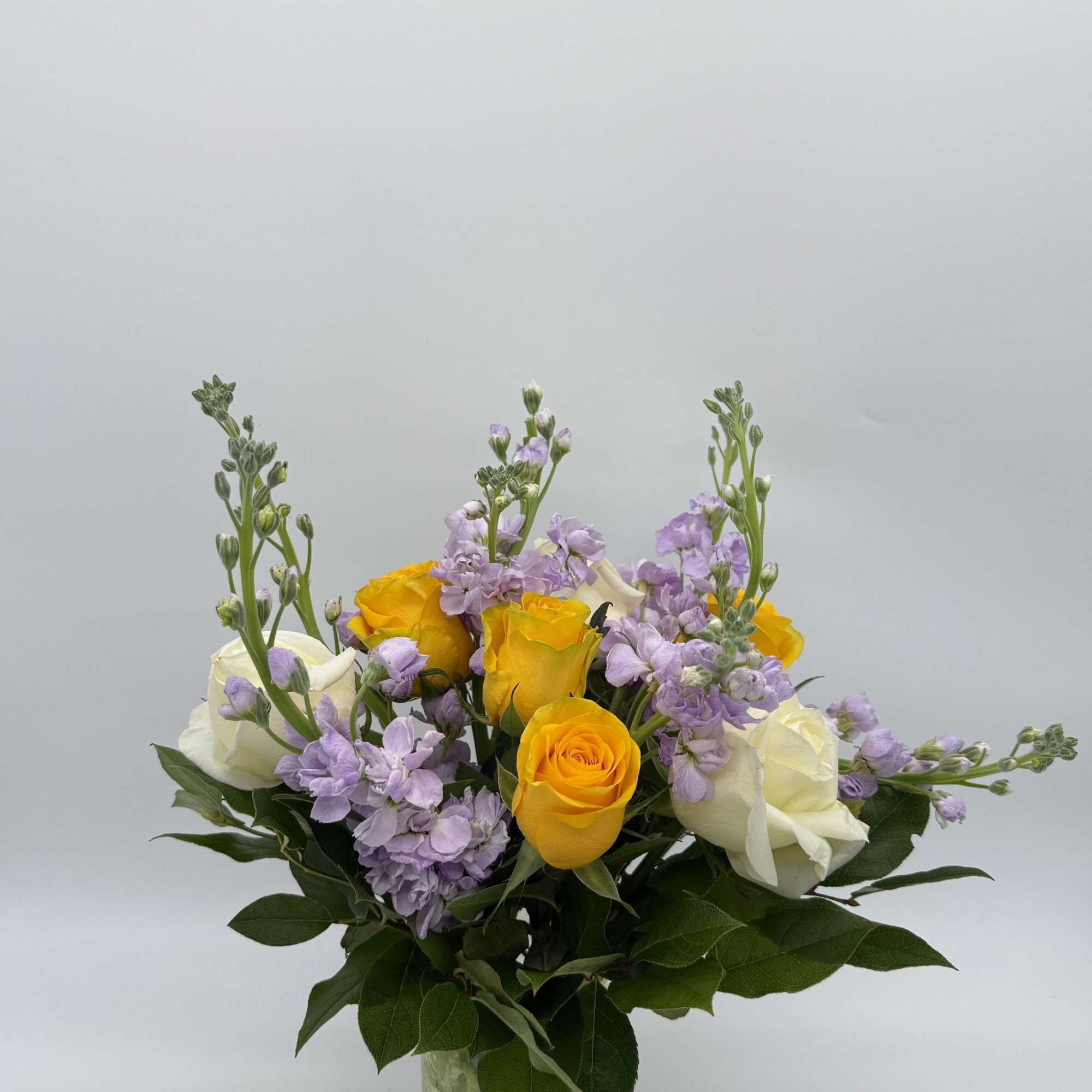 Yellow and white roses with lavender flowers in a glass vase