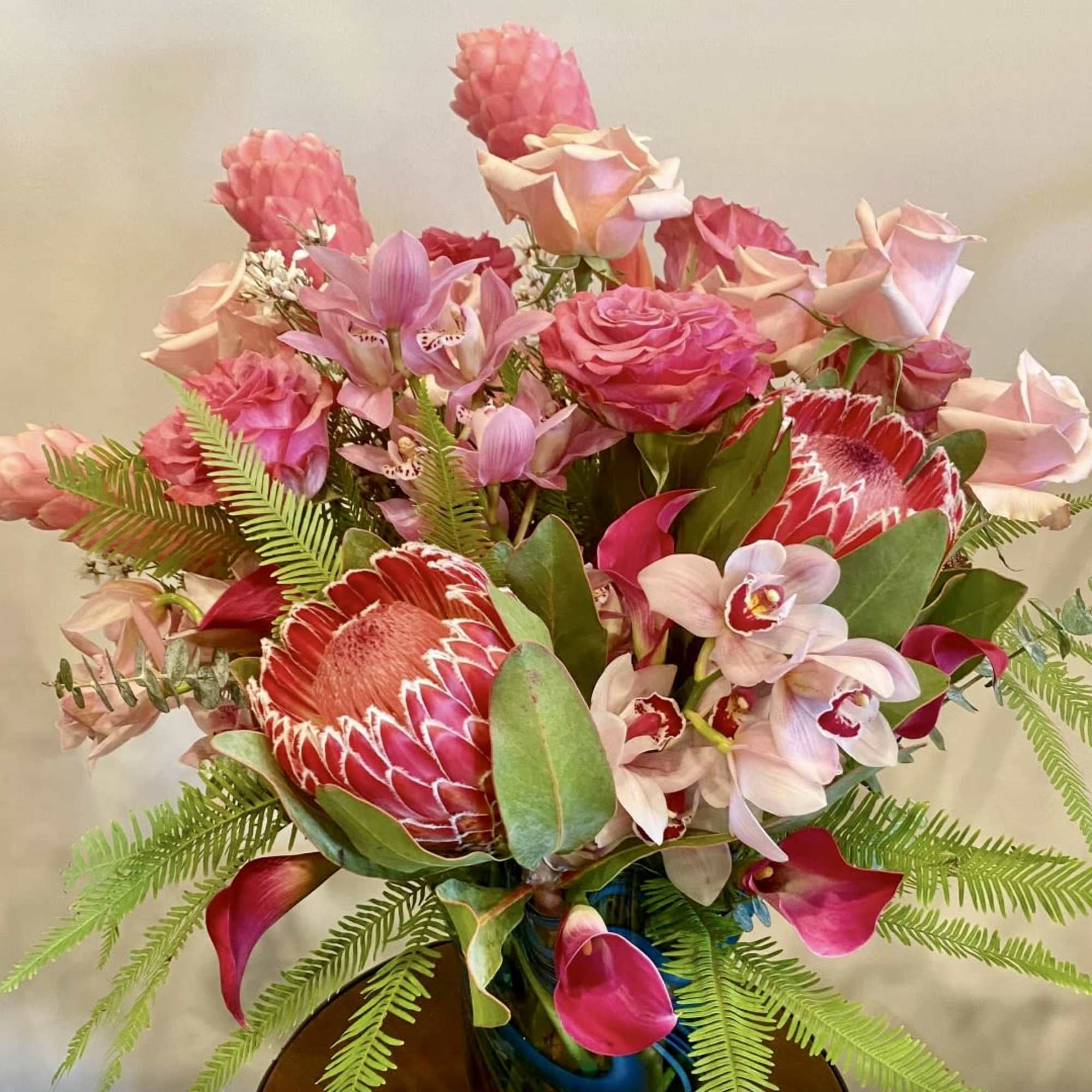 Pink and red tropical bouquet with roses, orchids, and protea in a vase