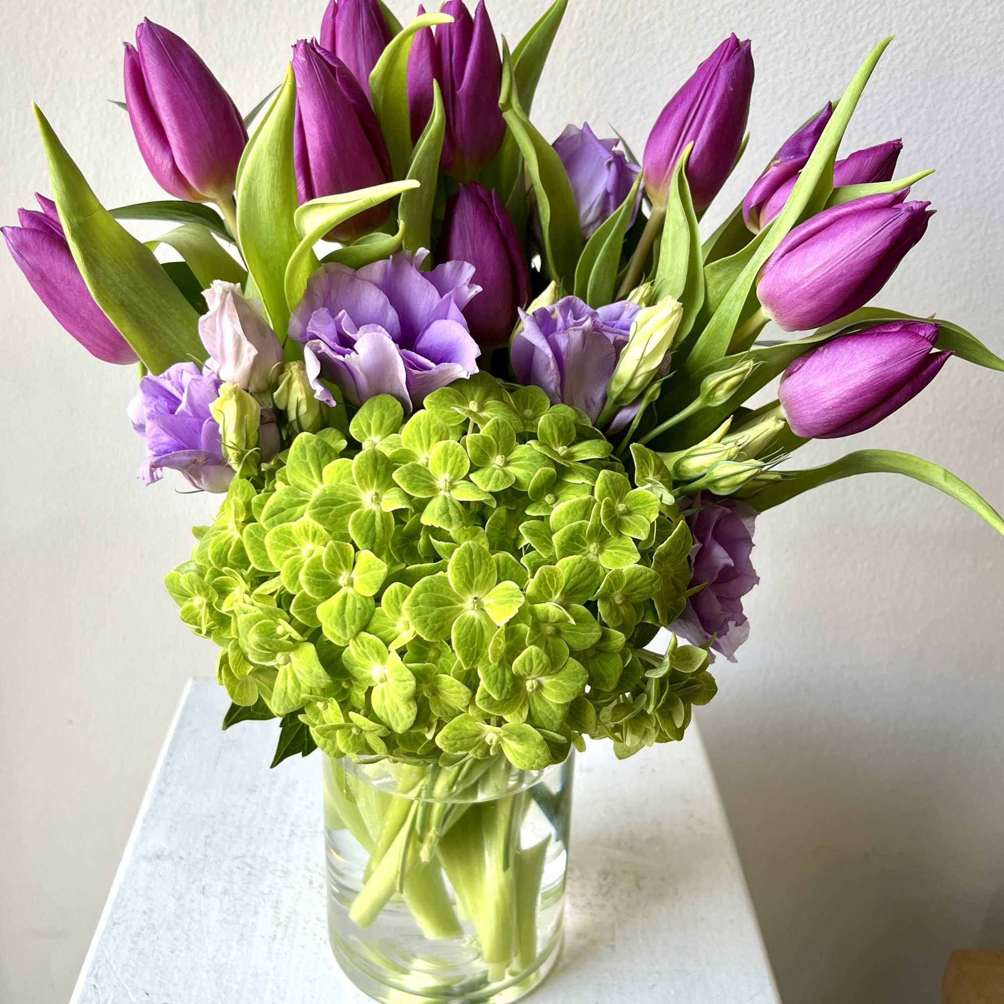 Purple tulips and lavender blooms in a clear glass vase with bright green hydrangea