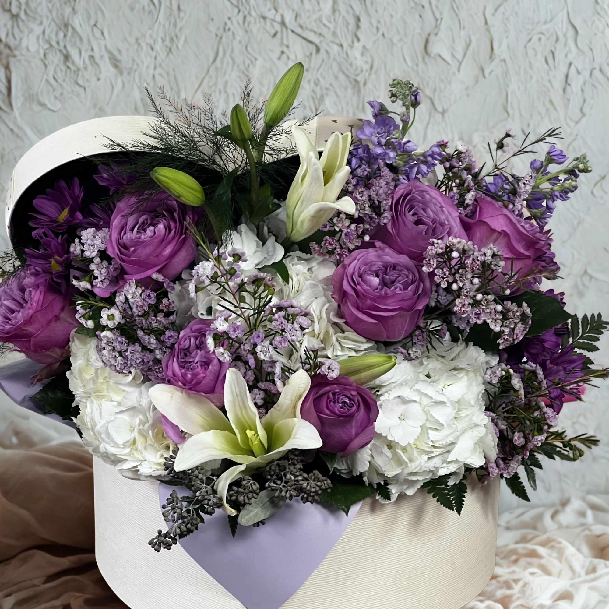 Purple roses, white hydrangeas and lilies with lavender filler, arranged in a