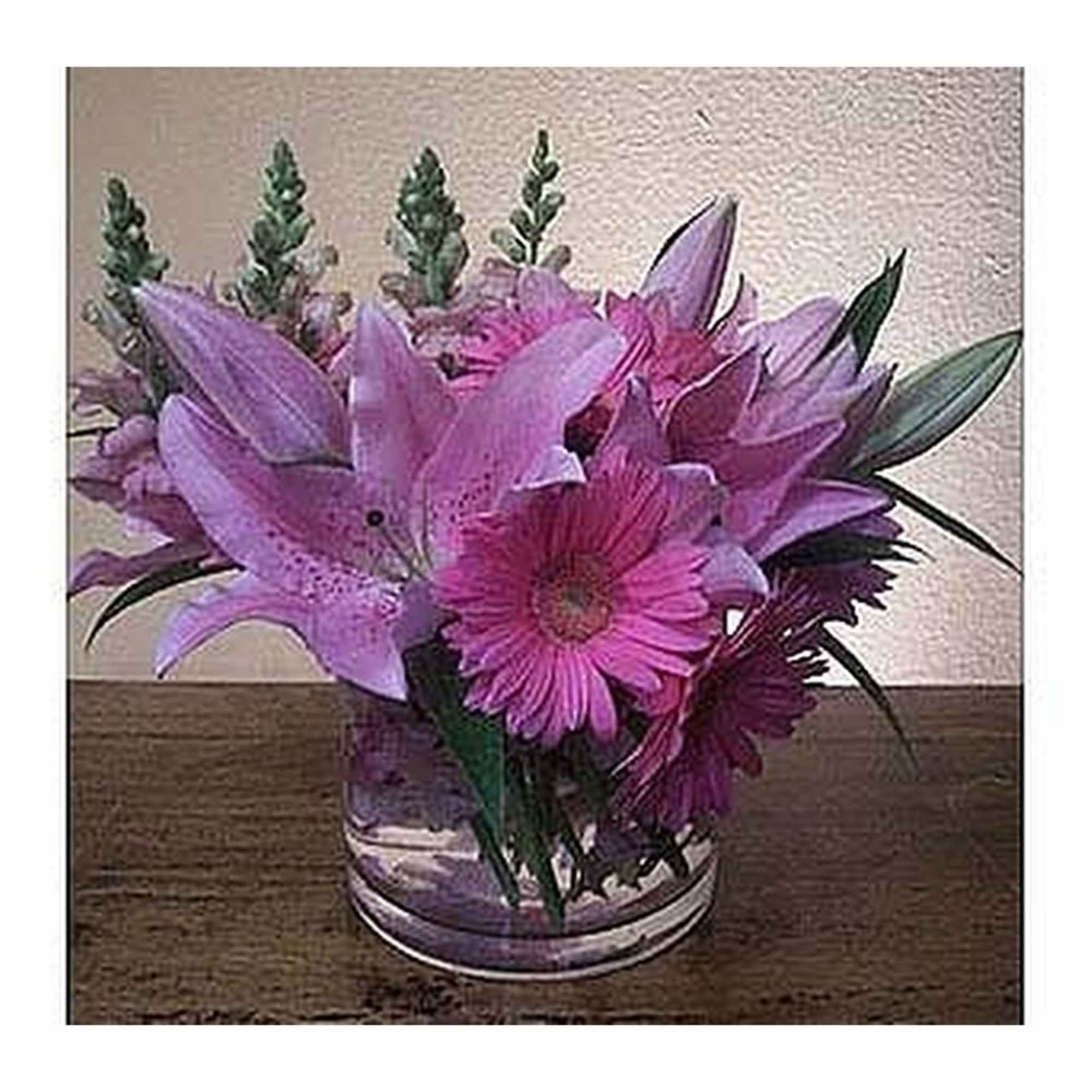 Low arrangement of pink lilies and gerbera daisies in a clear glass vase on a wooden surface