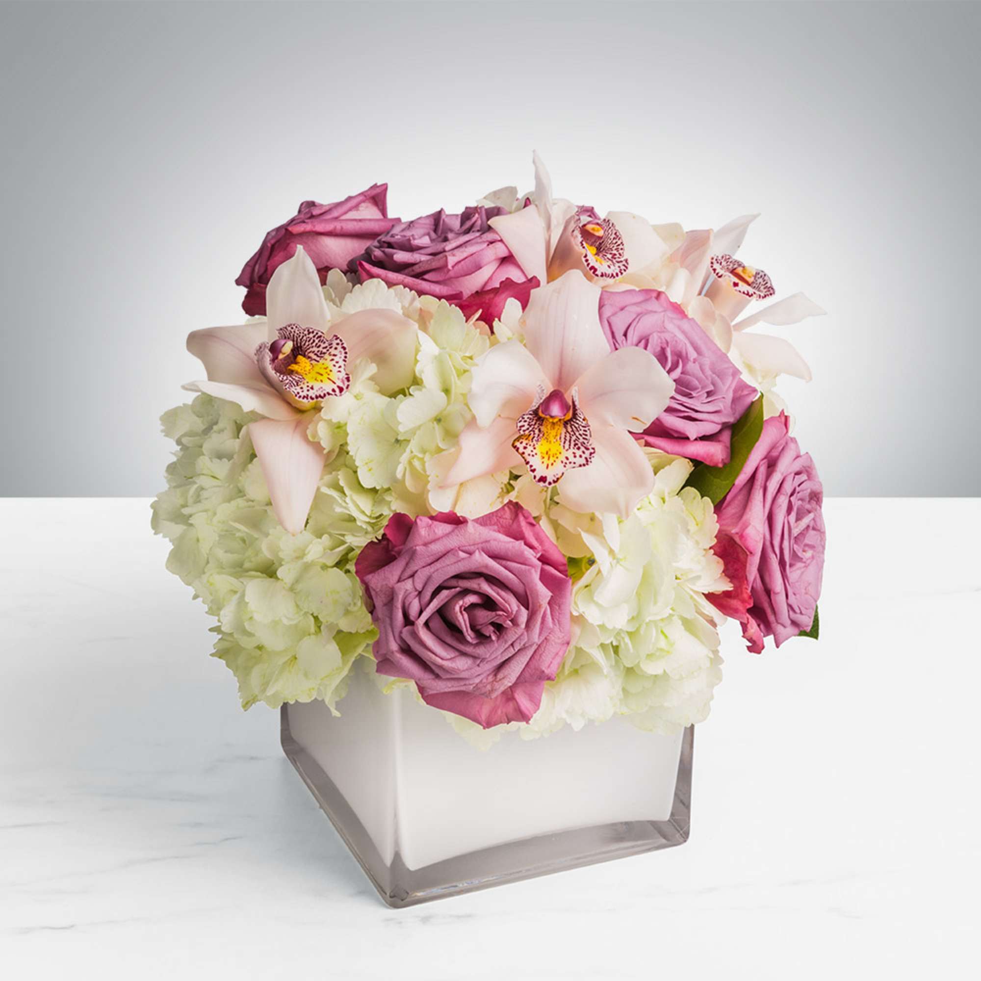 Pink roses and pale orchids arranged in a square glass vase
