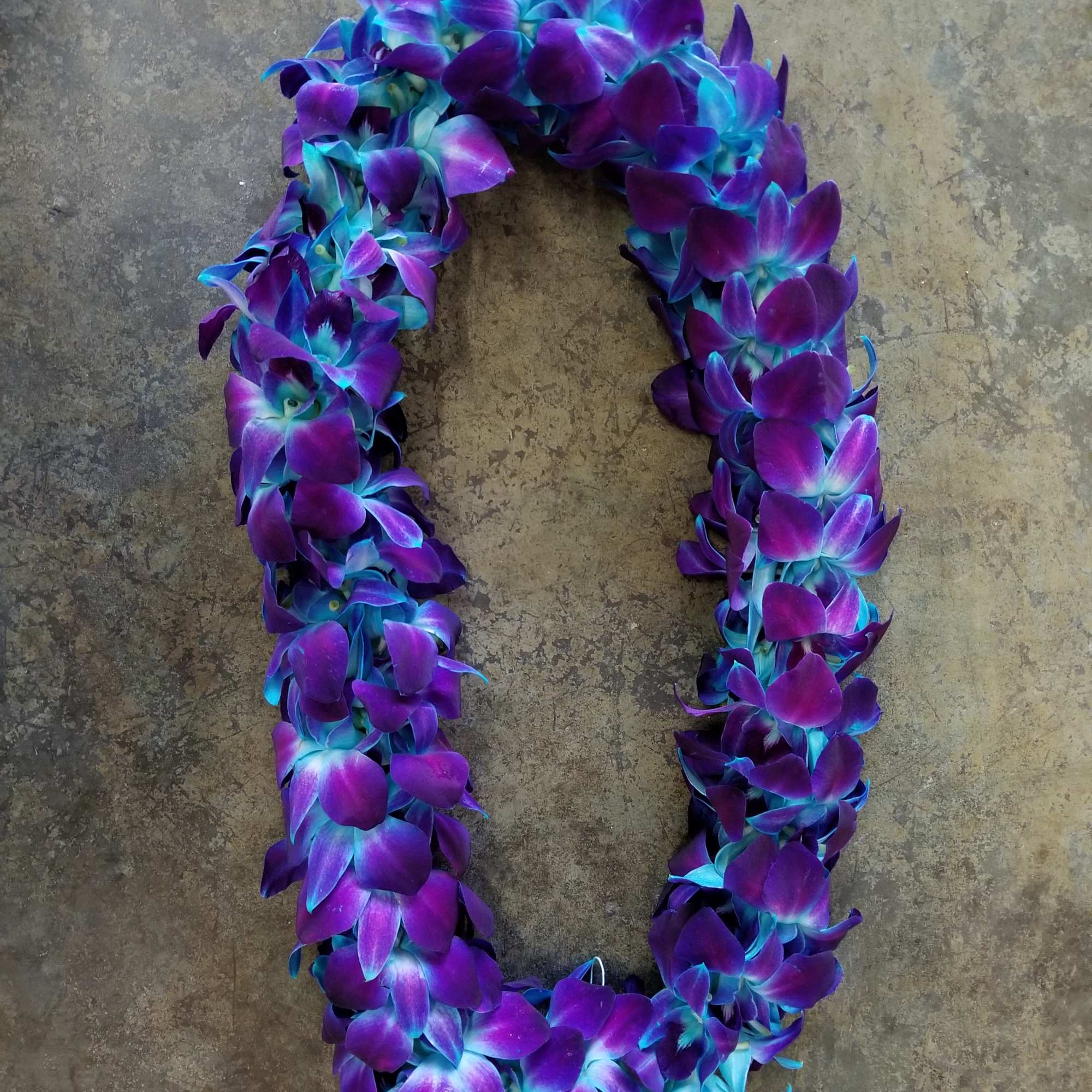 Purple and blue orchid lei on a stone surface