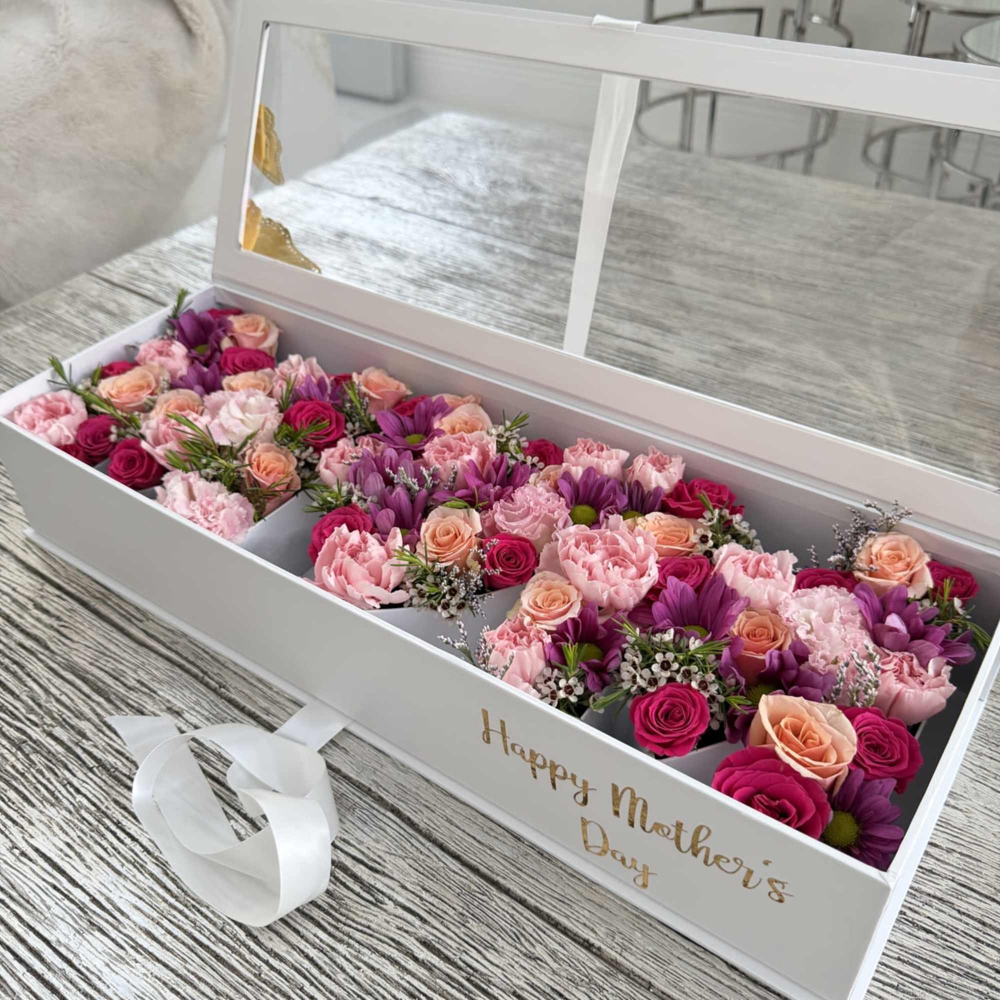 A long white gift box filled edge-to-edge with pink, peach, lavender, and