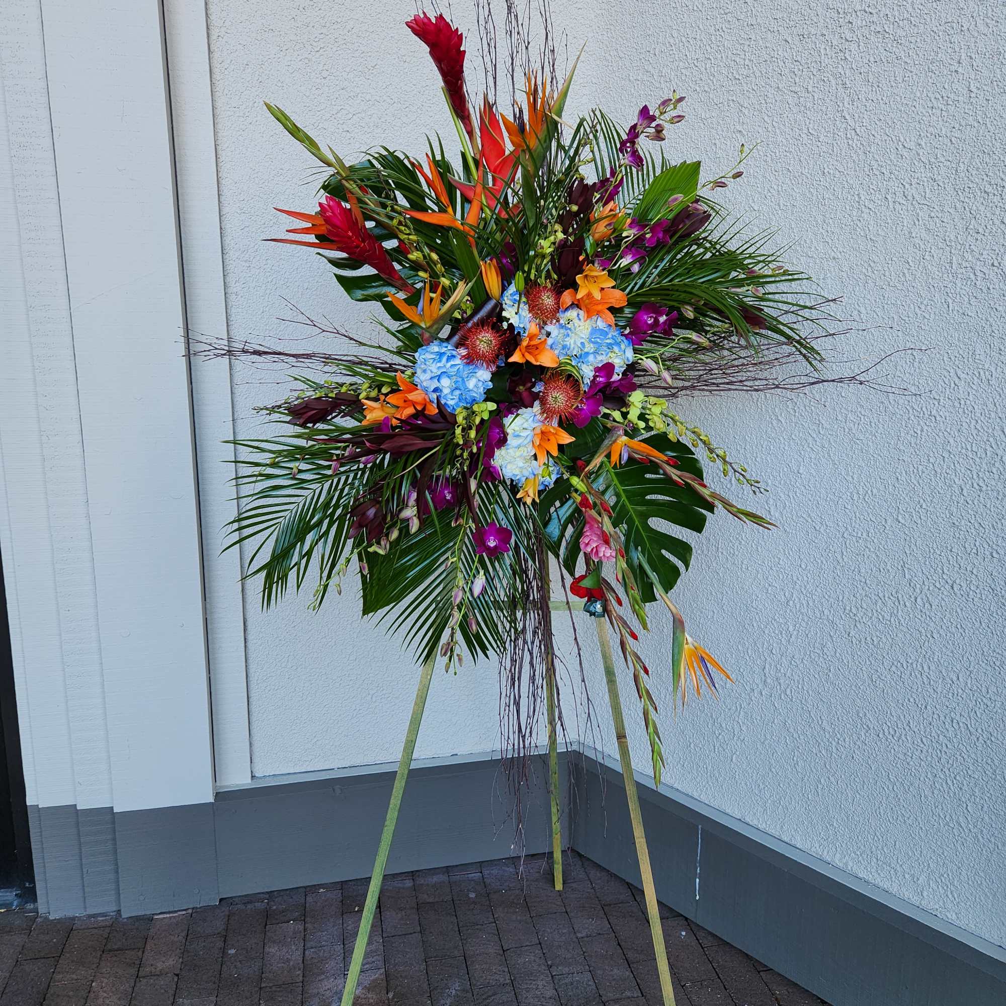 Tall tropical floral standing spray with bright mixed blooms on a tripod easel