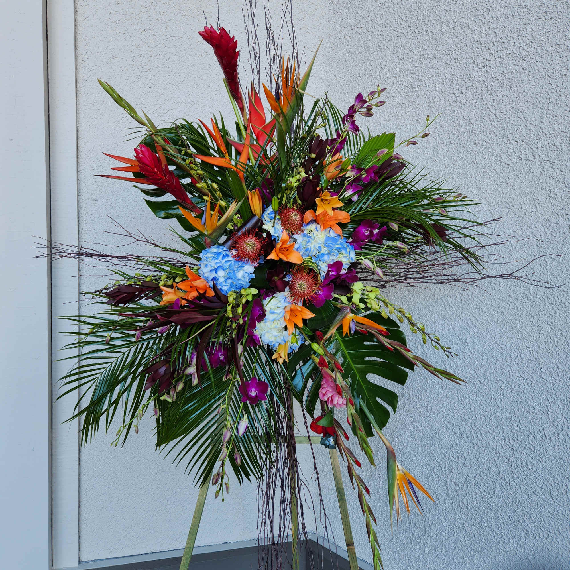Tall tropical flower arrangement with orange, purple, blue, and red blooms on a stand