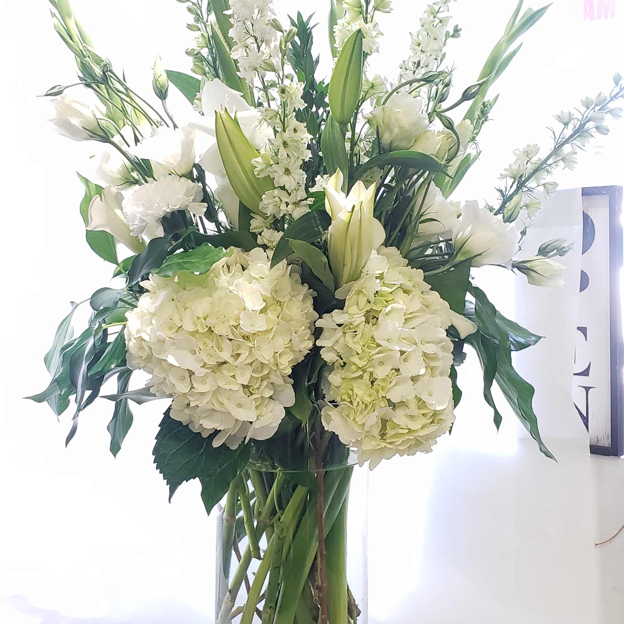 White floral arrangement in a tall glass vase with lilies and hydrangeas