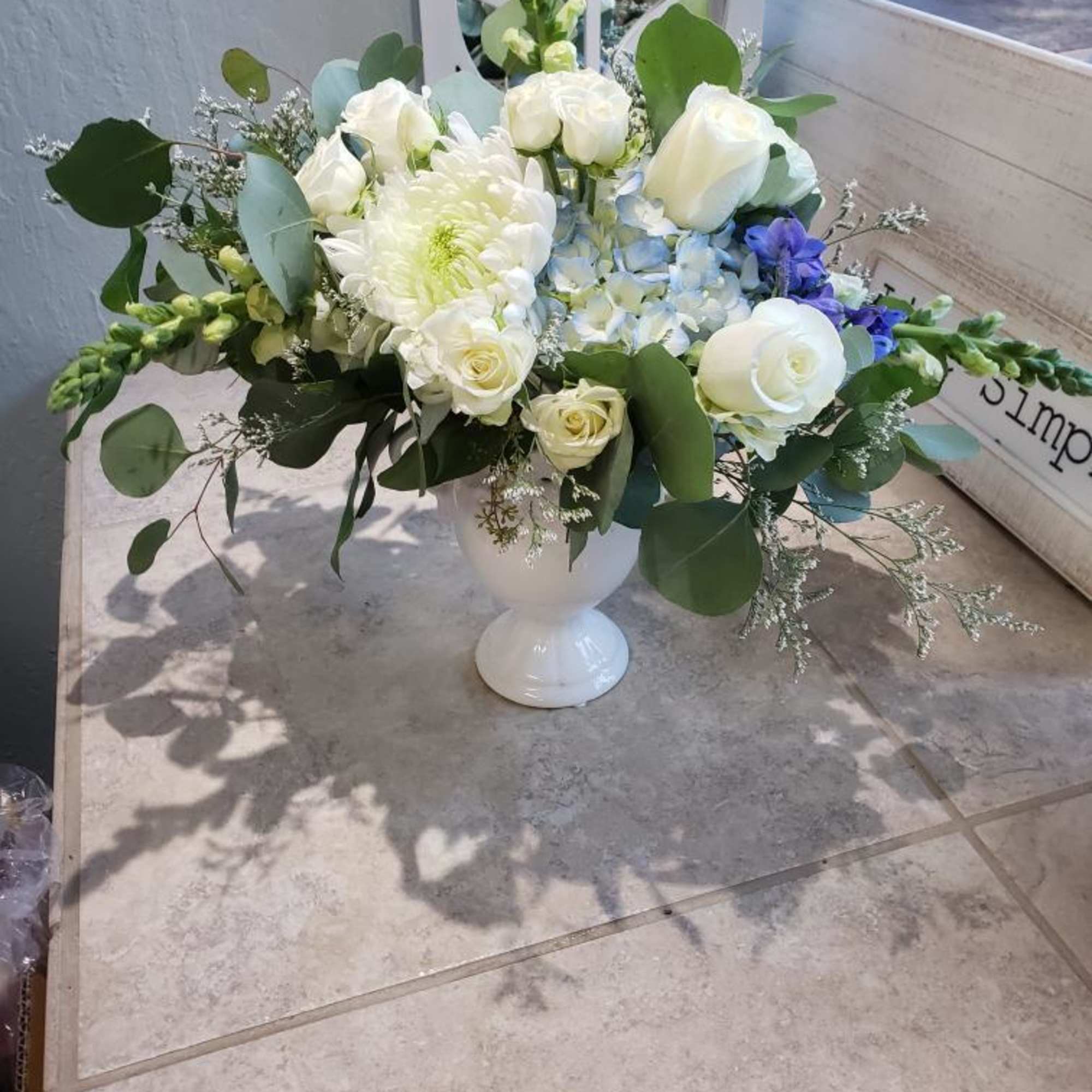 White floral arrangement in a white pedestal vase with blue accents