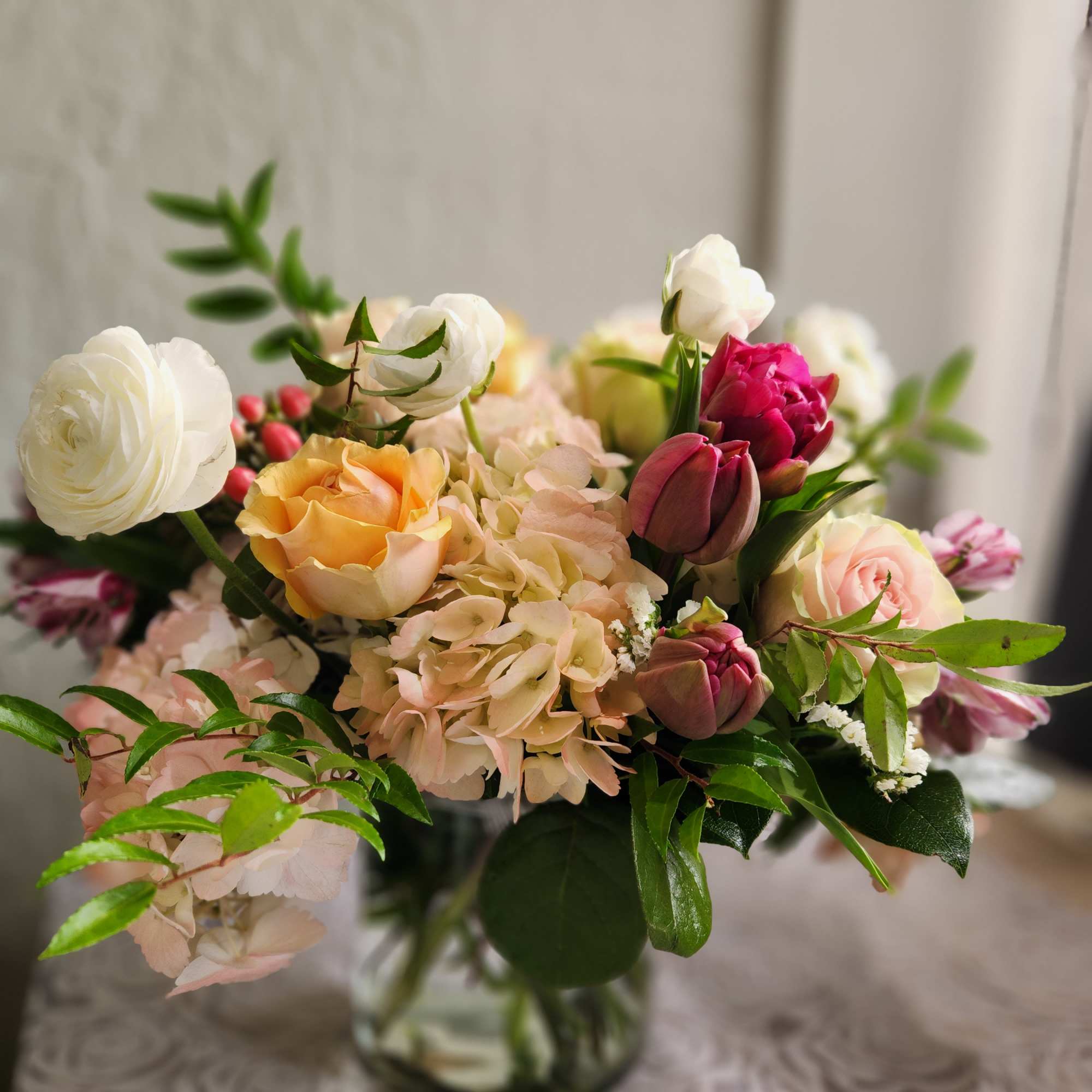 Mixed bouquet of roses, hydrangeas, and tulips in a glass vase