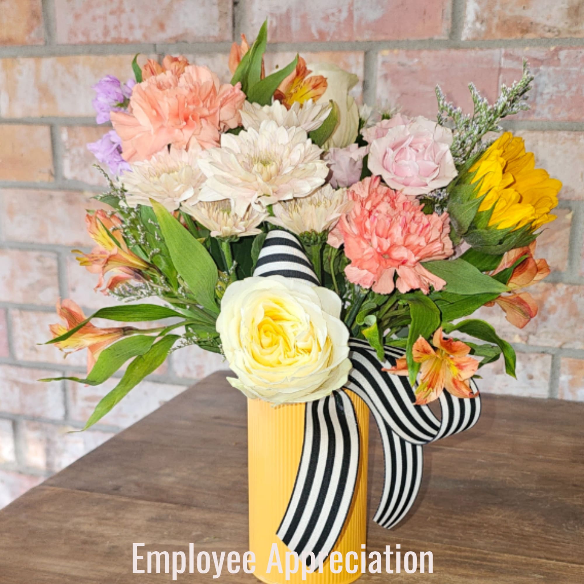 Mixed bouquet in a yellow vase with striped ribbon and pastel flowers including a yellow rose and sunflower