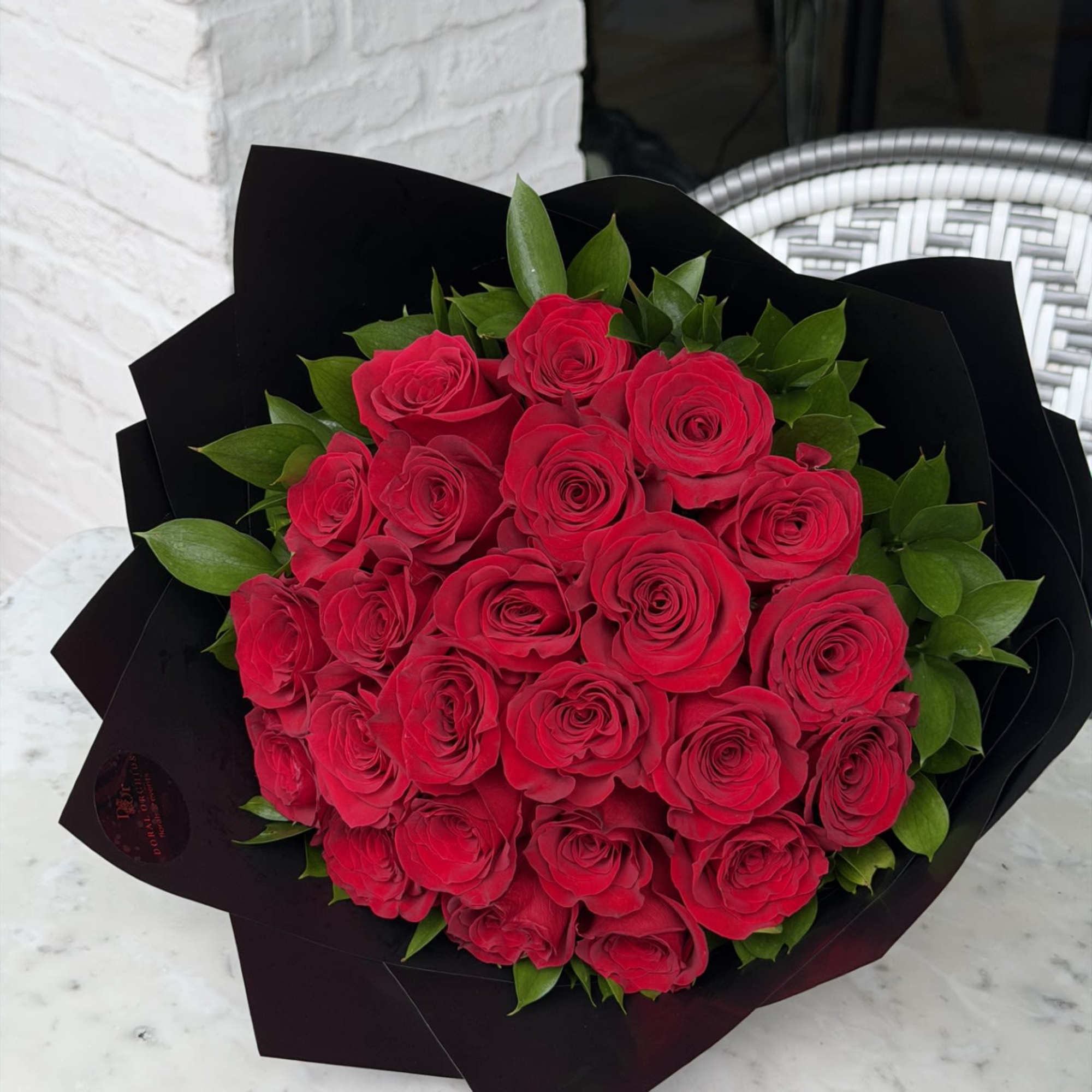 A dramatic bouquet of 24 velvety red roses wrapped in sleek black