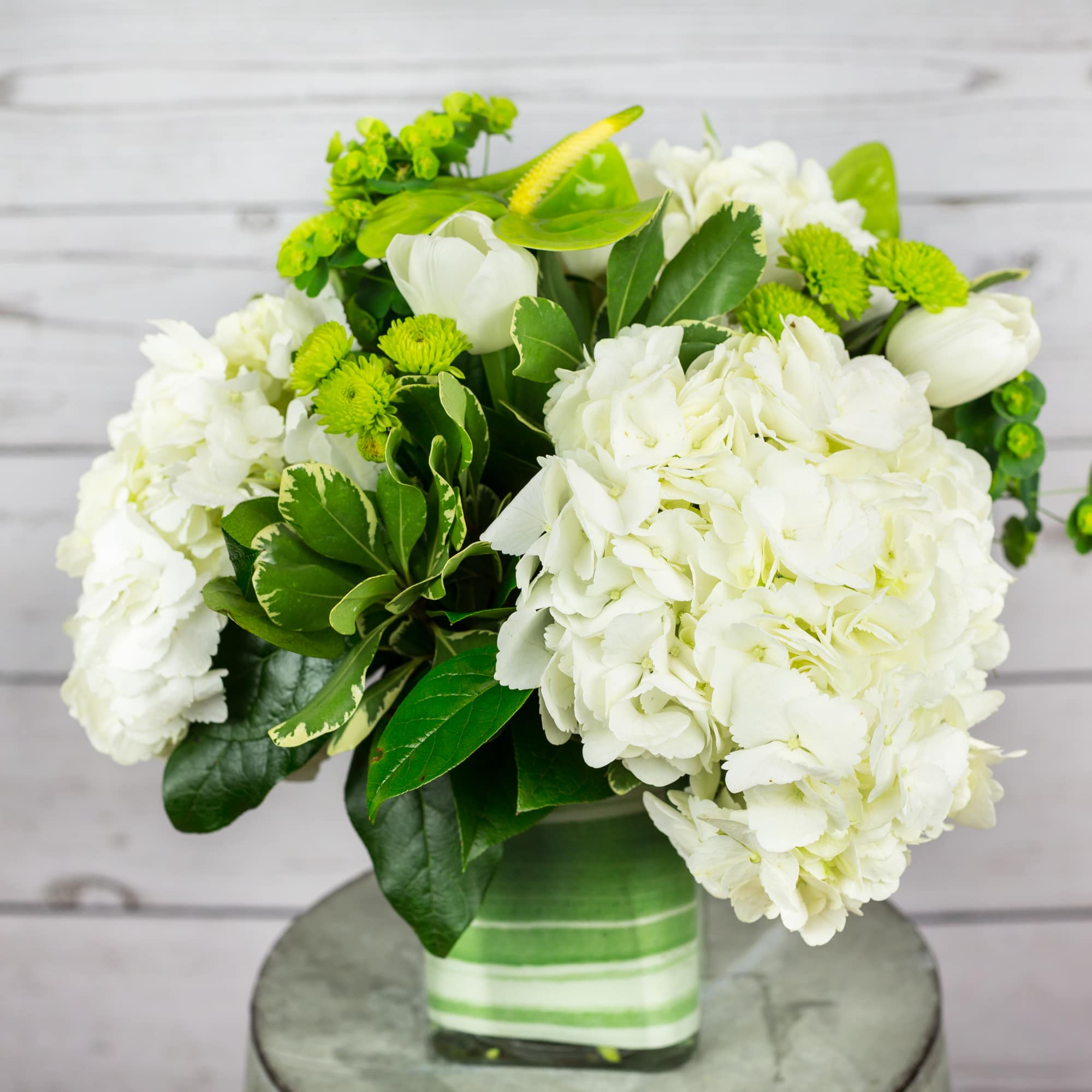 White hydrangeas and green flowers in a striped glass vase