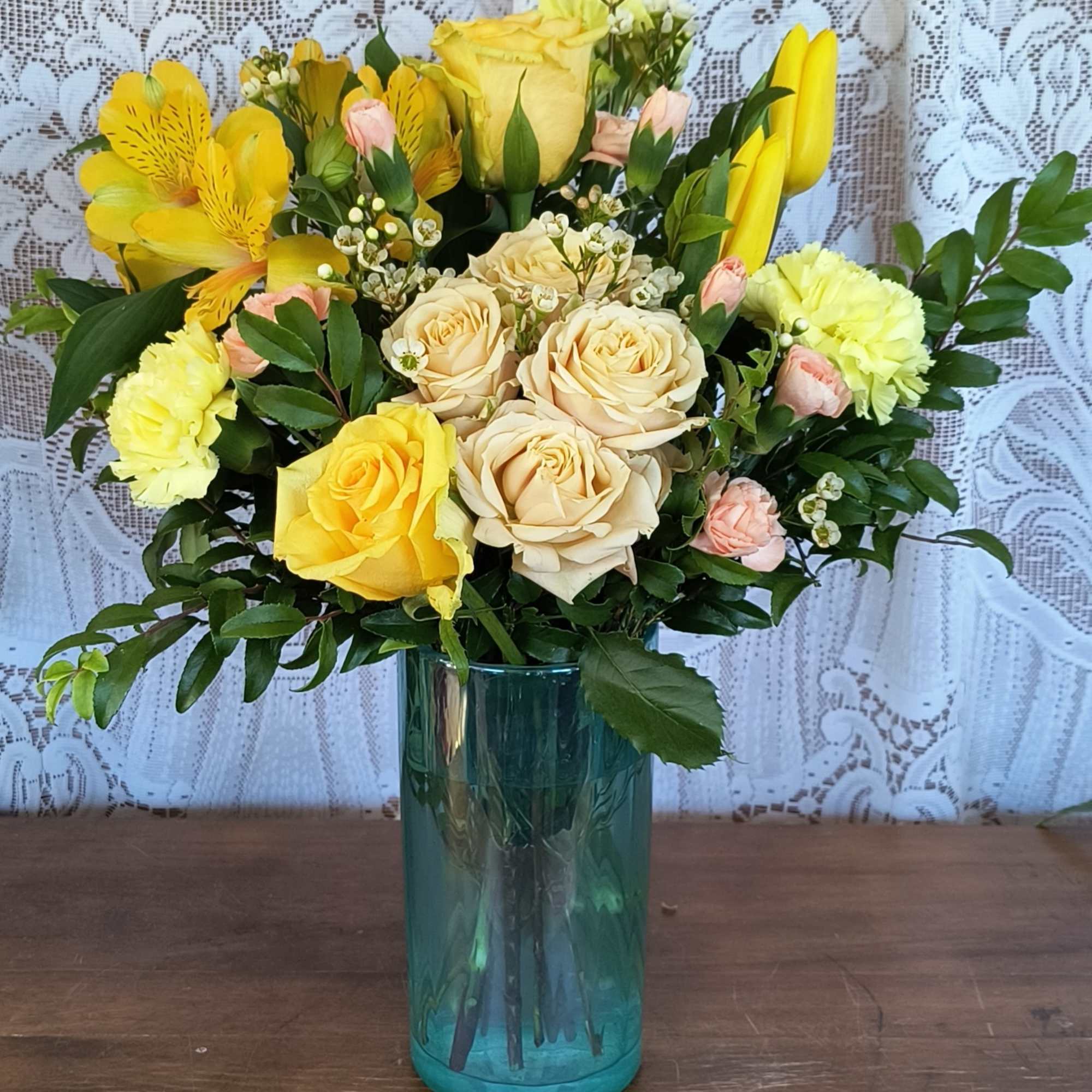 Yellow and cream roses with pink accents in a blue glass vase