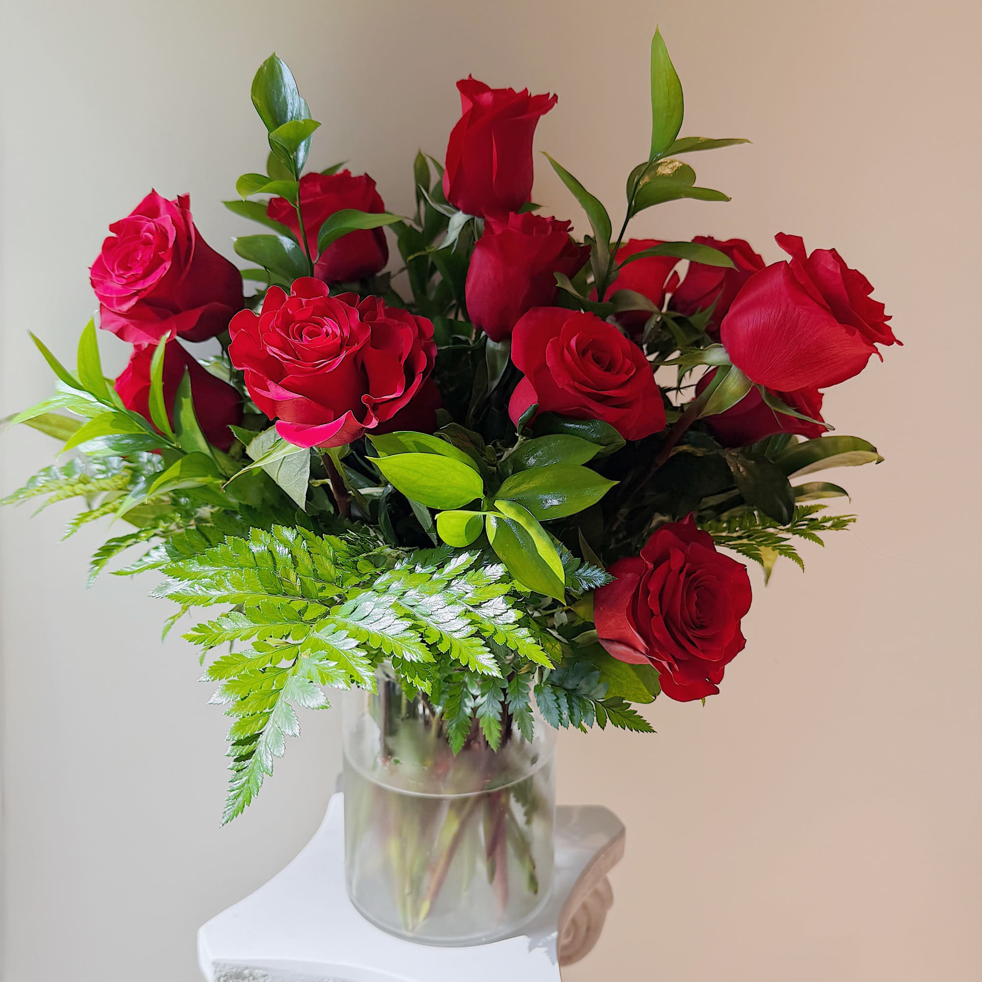 Red roses arranged in a clear glass vase with fern foliage