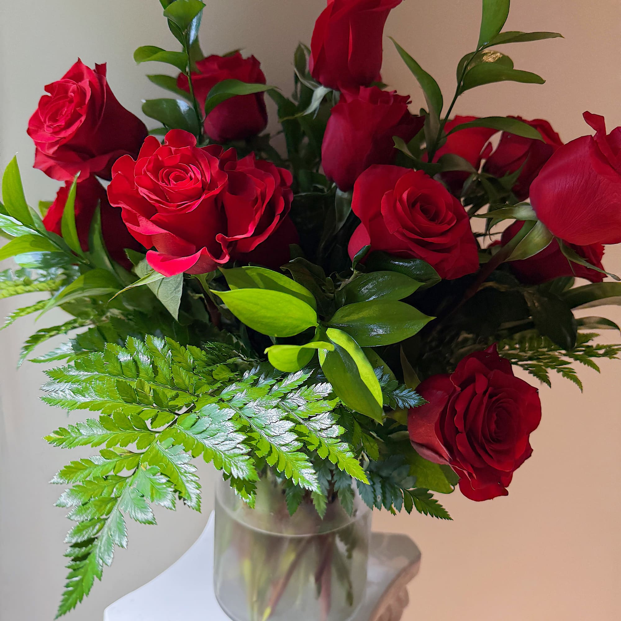 Red roses arranged in a clear glass vase with fern foliage