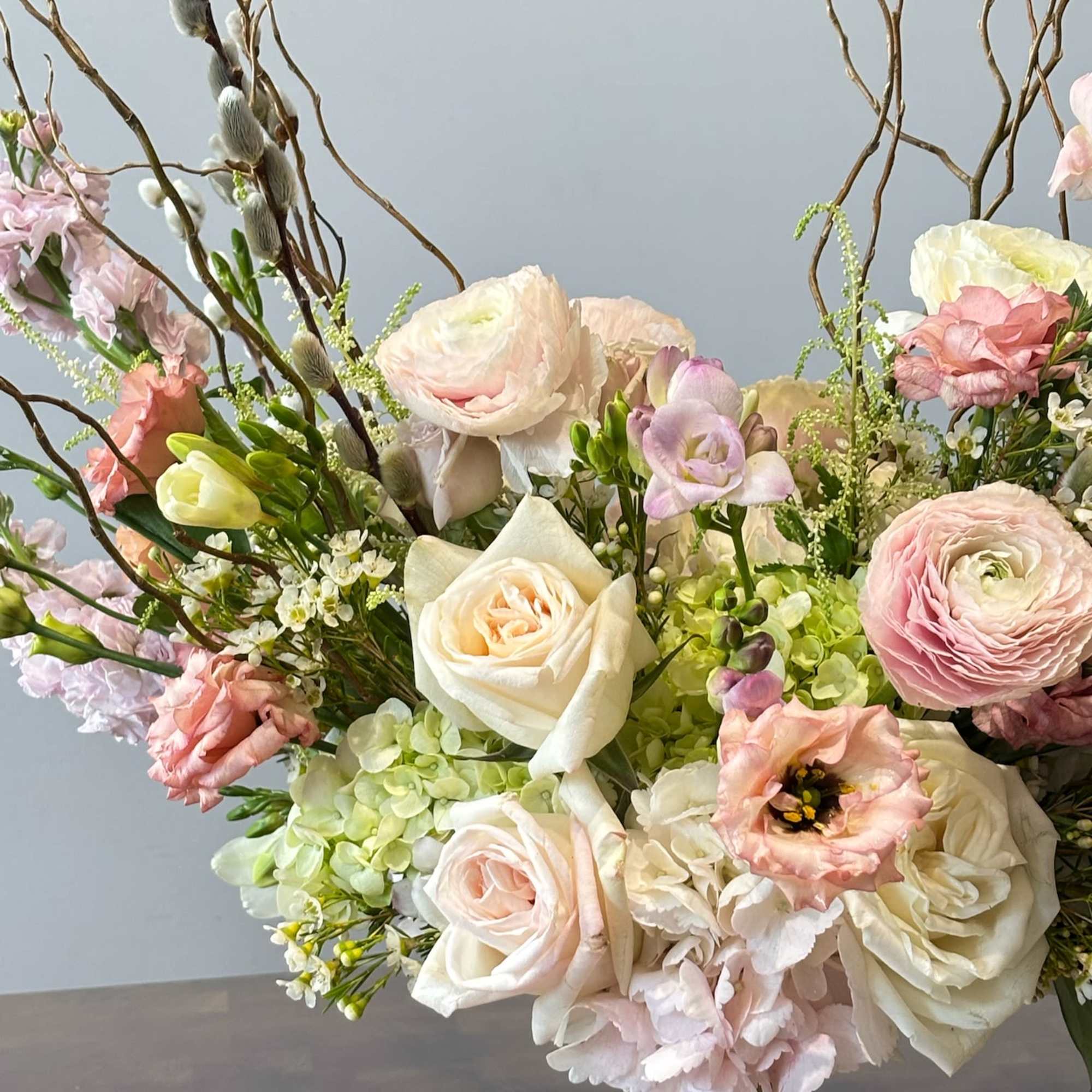 Pastel floral arrangement with roses, ranunculus, and lisianthus in a gold vase