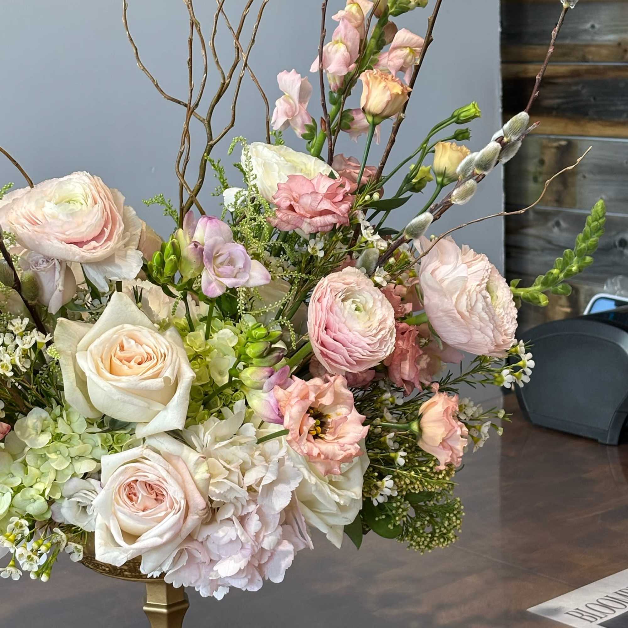 Pastel floral arrangement with roses, ranunculus, and snapdragons in a gold vase