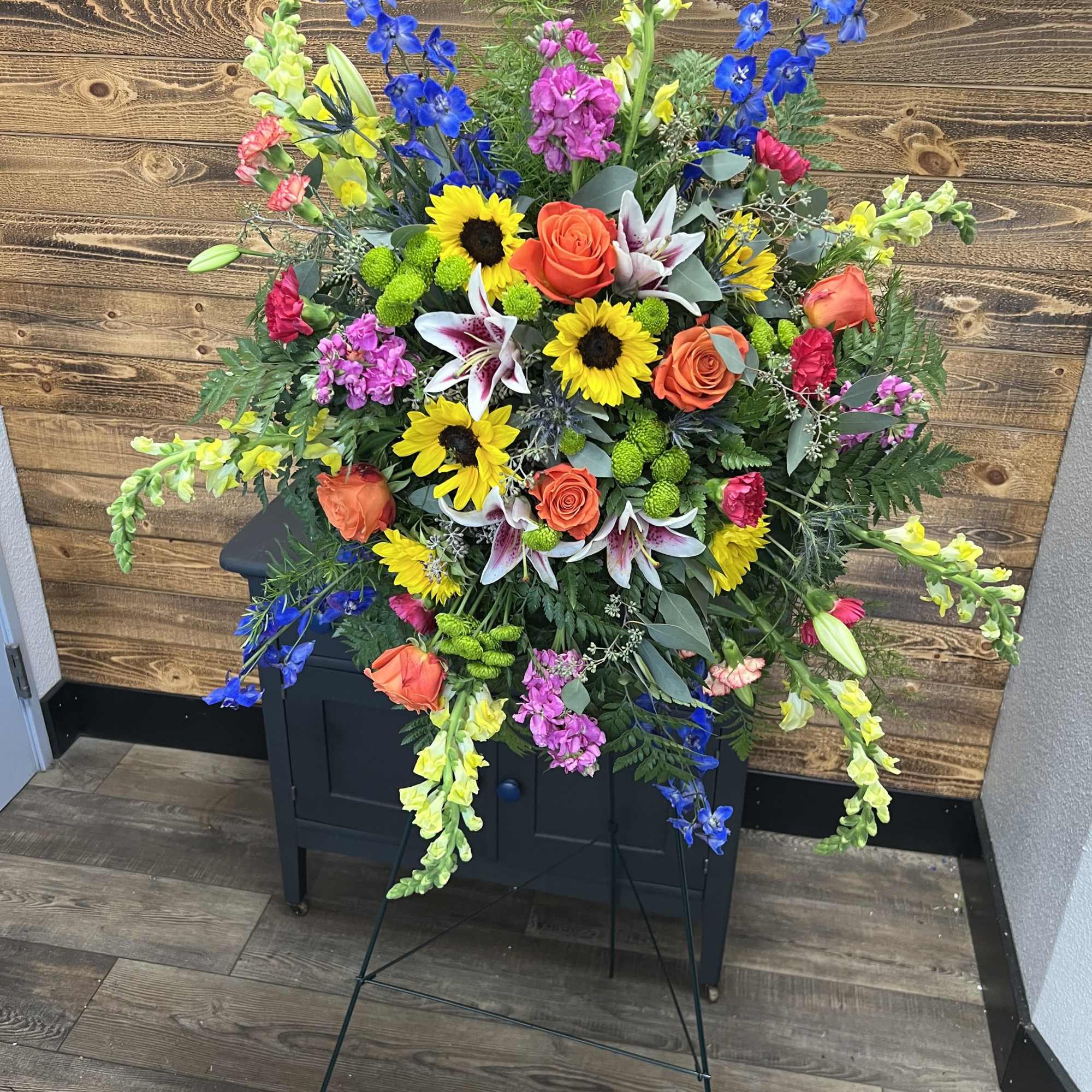 Large standing floral spray with sunflowers, roses, lilies, and blue delphinium