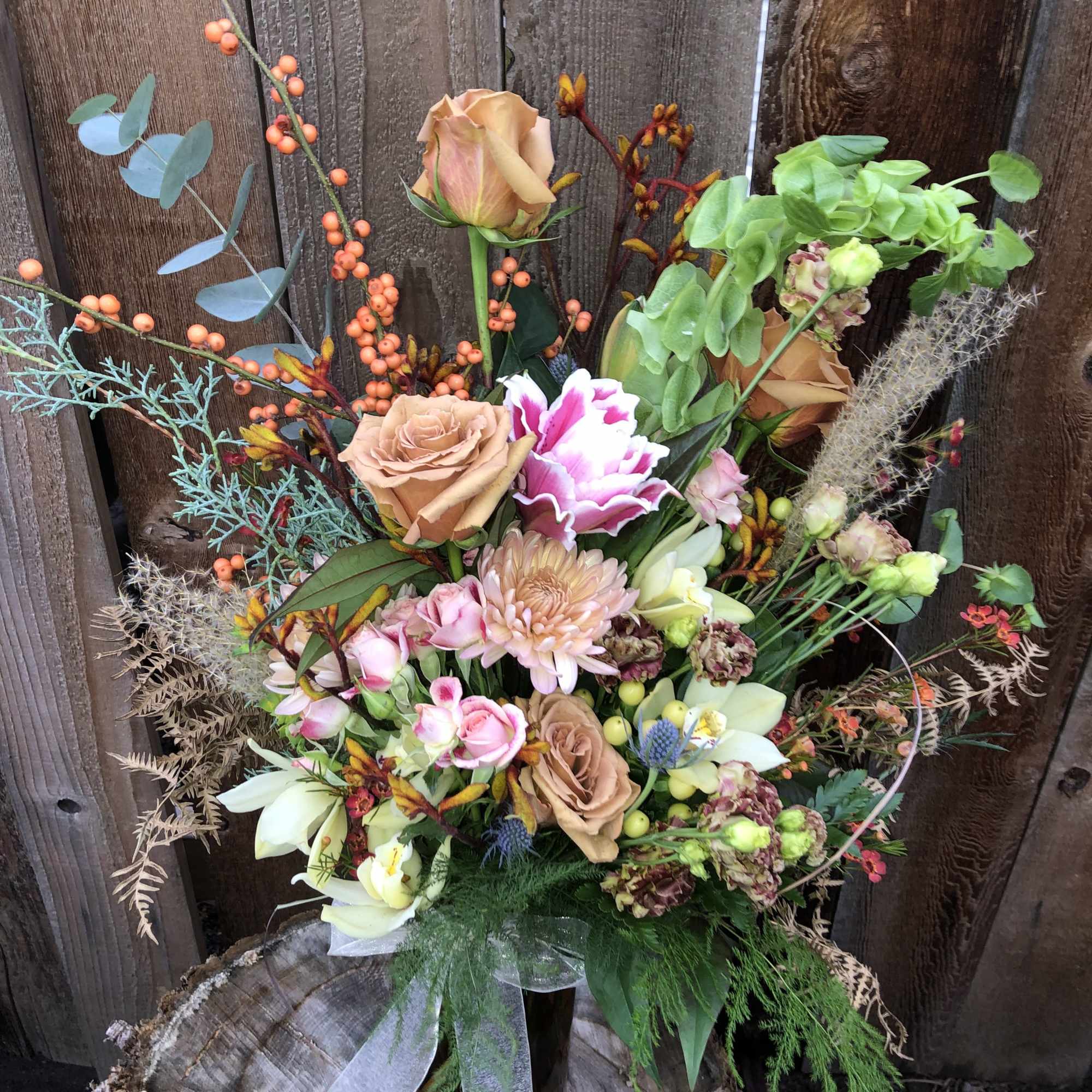 Tall mixed bouquet with peach roses, pink spray roses, and green orchids in a glass vase