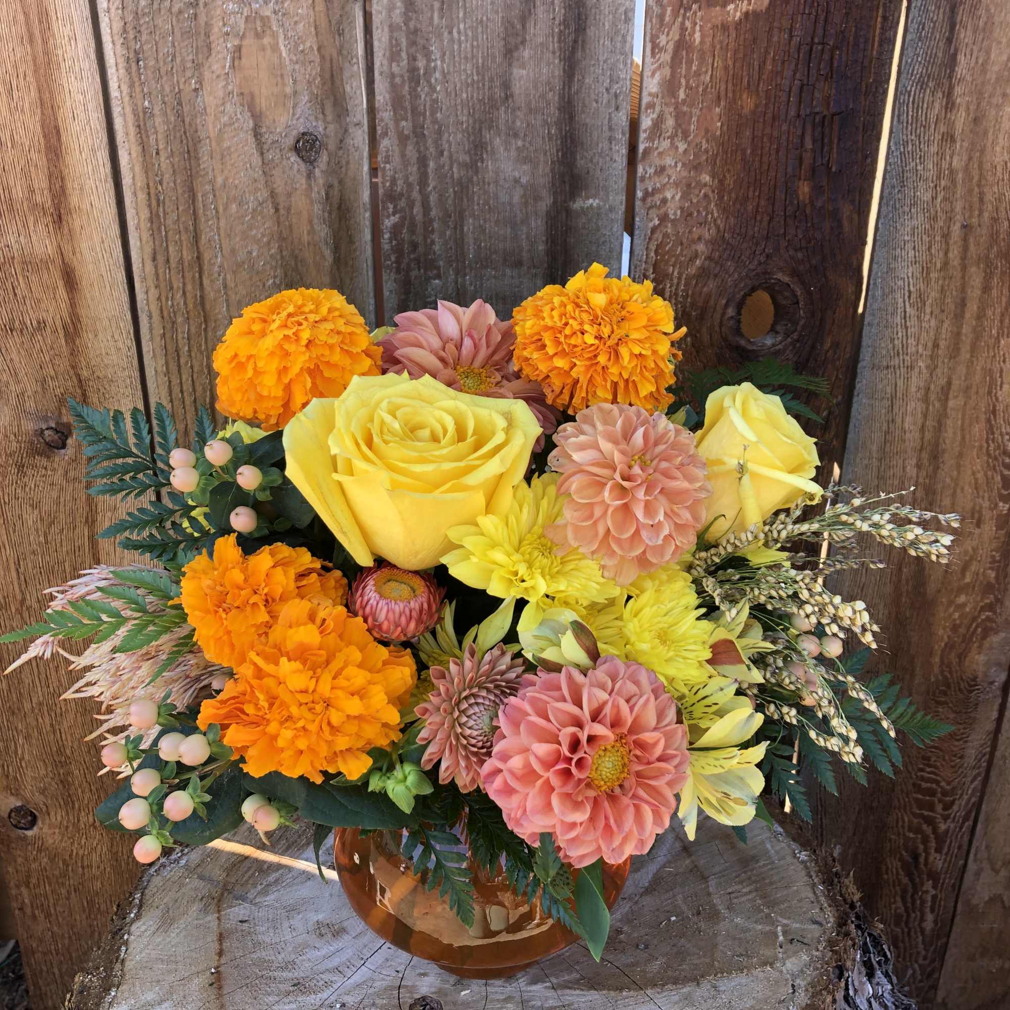 Bouquet of yellow roses, orange marigolds, and pink dahlias in an amber vase