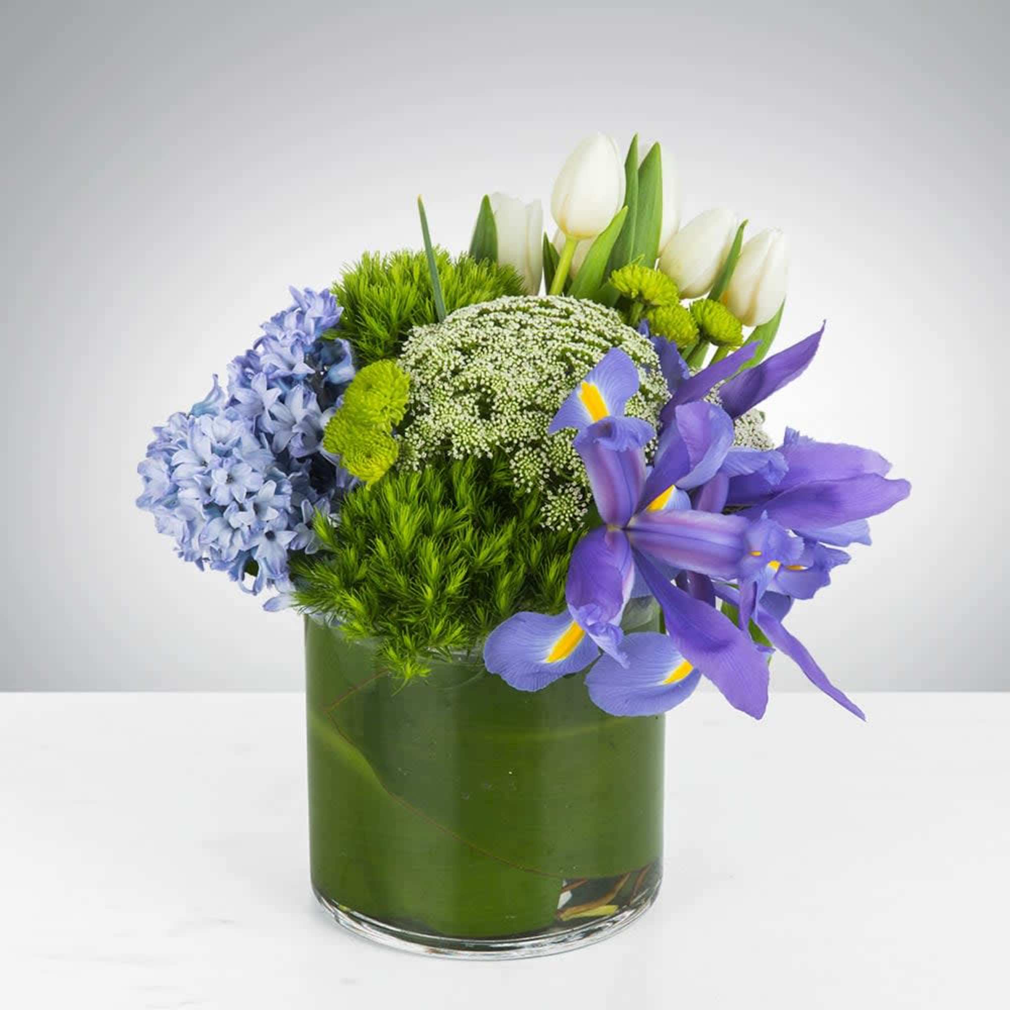 This arrangement includes green dianthus, blue iris, white tulips, hyacinths, and other